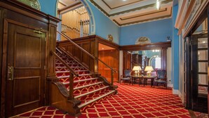 A grand staircase with a red carpet leading to a room with blue walls and a chandelier. - The Metropole Hotel (Blackpool)