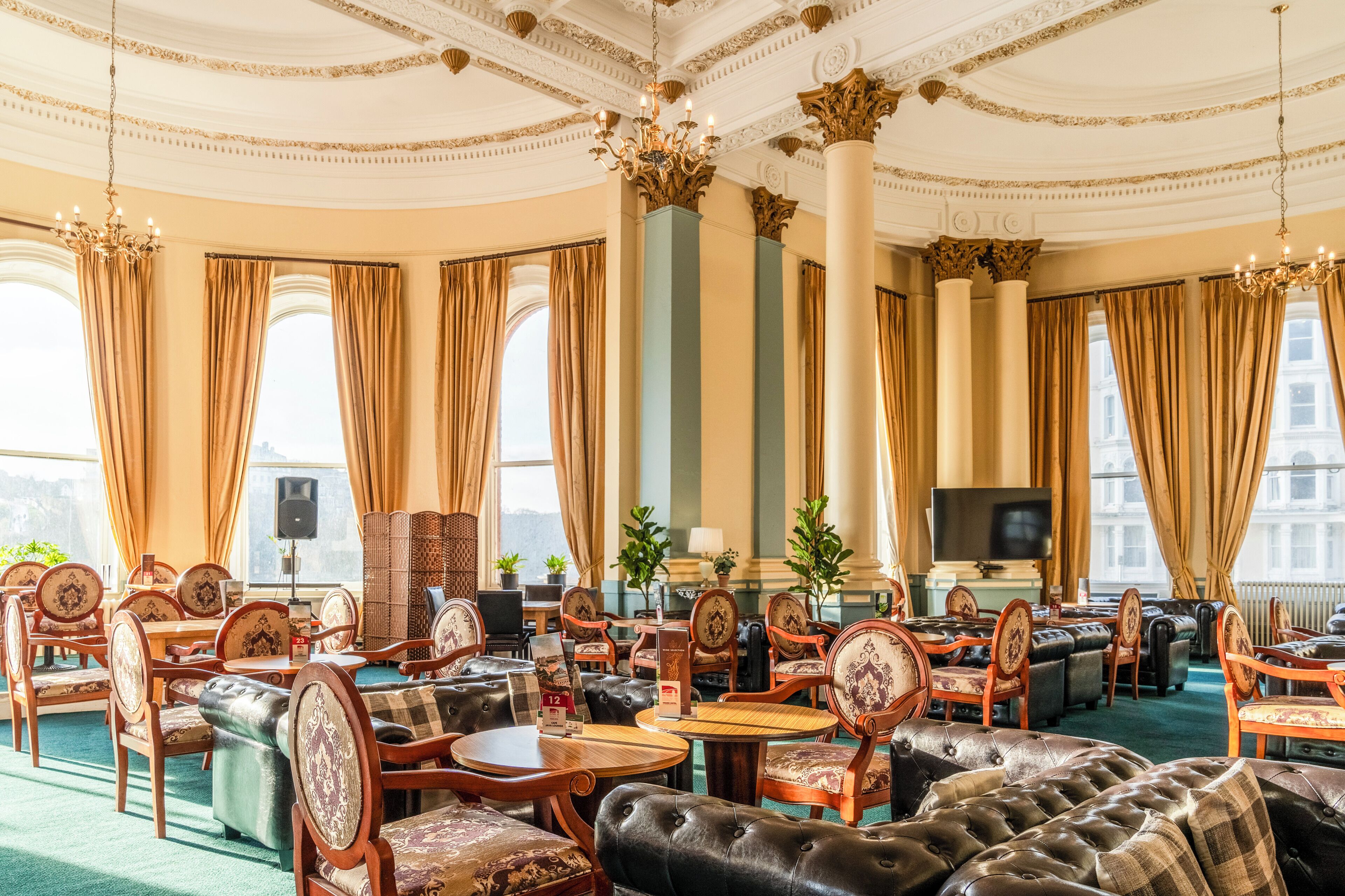 A luxurious hotel lobby with ornate chandeliers, plush seating, and large windows offering city views.