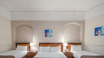 A hotel room with three beds, a wooden headboard, a painting of a lighthouse, and a white ceiling.