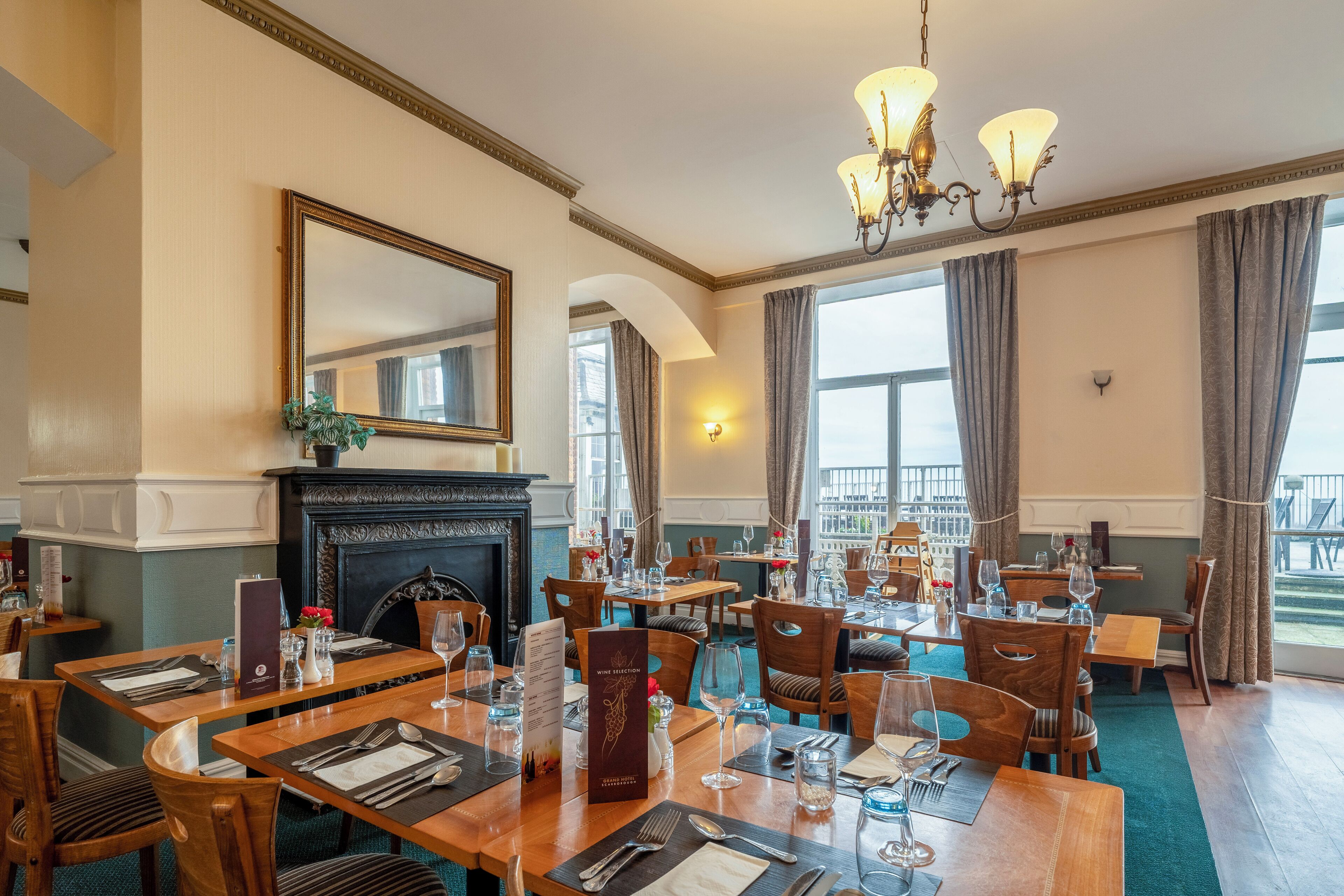 Une salle à manger avec plusieurs tables dressées pour les invités, une cheminée et un grand miroir au mur.