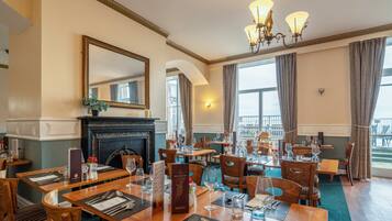 A dining area with multiple tables set for guests, a fireplace, and a large mirror on the wall.