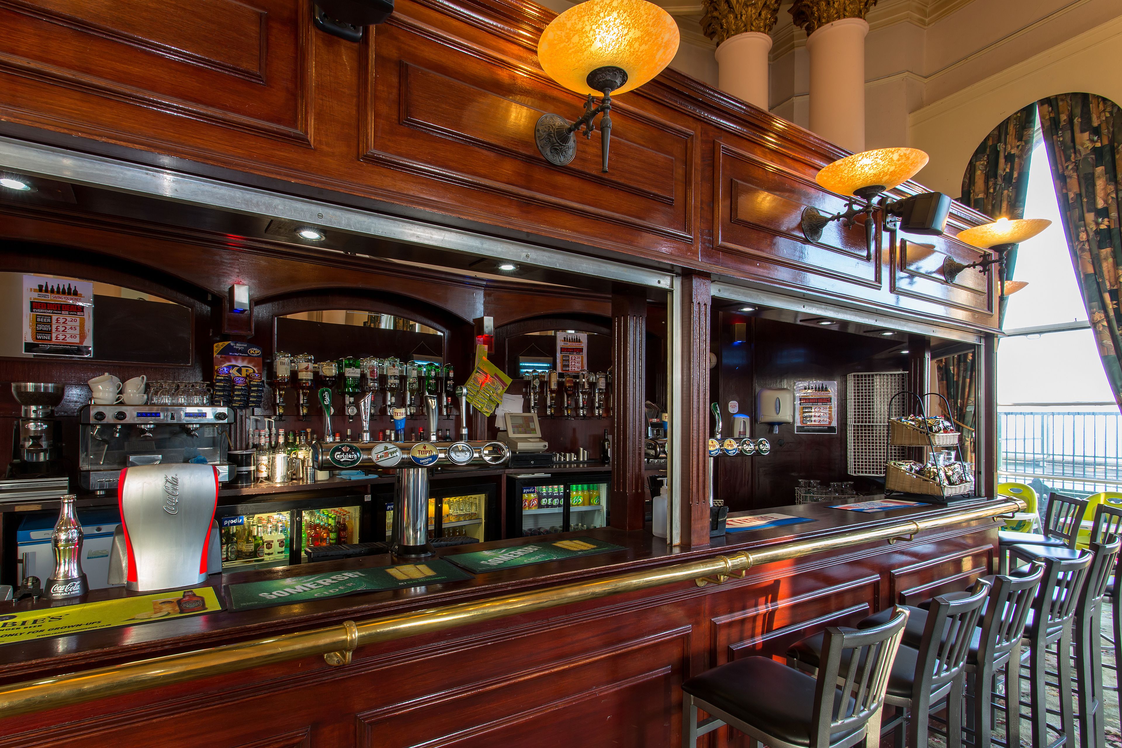 Un bar con paneles de madera, una caja registradora y una variedad de botellas y vasos.