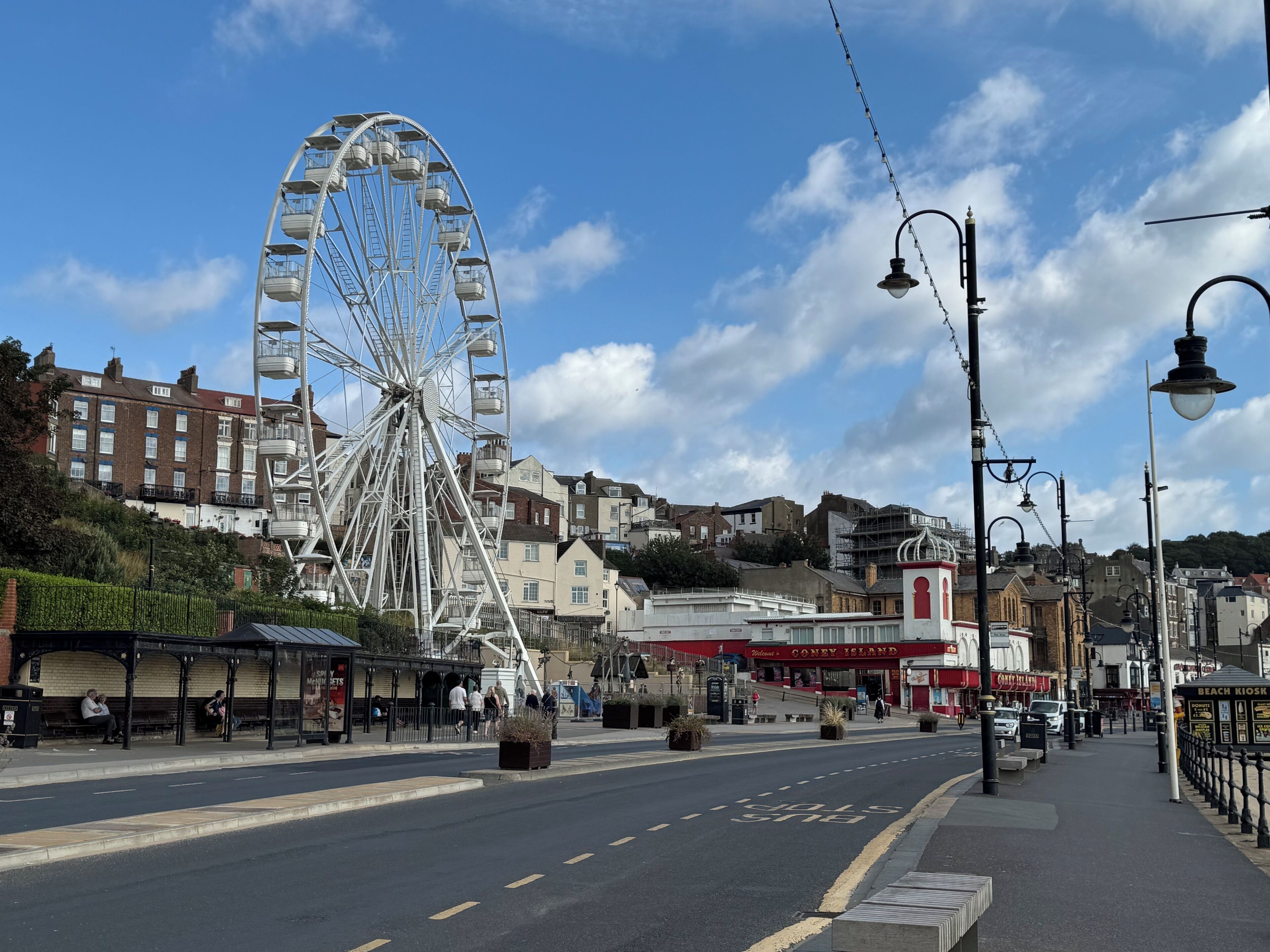 A street with a Ferris wheel, a bus stop, and a building with a red awning.