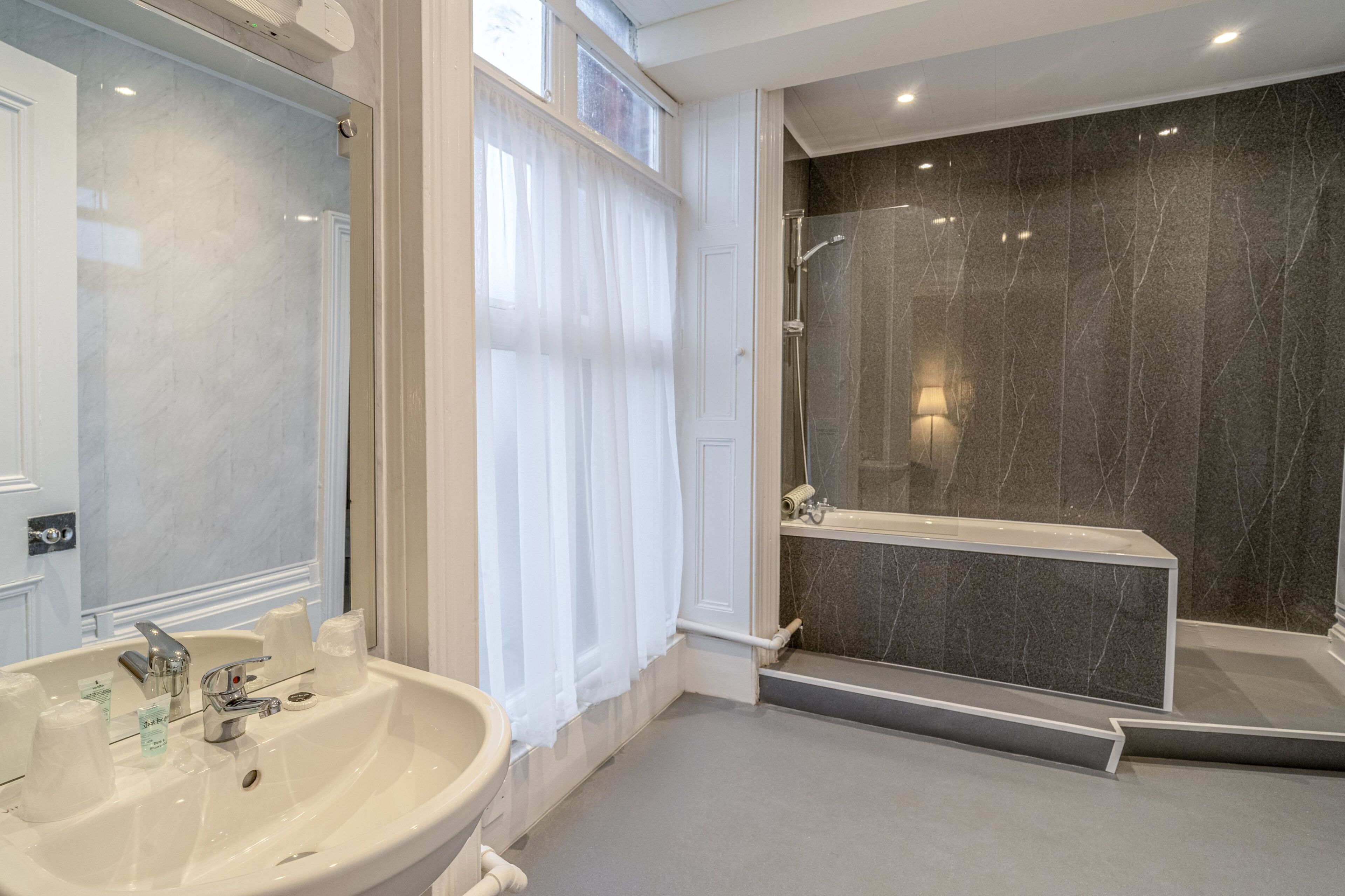 Ein Badezimmer mit Waschbecken, Spiegel, Dusche und Marmorwänden.