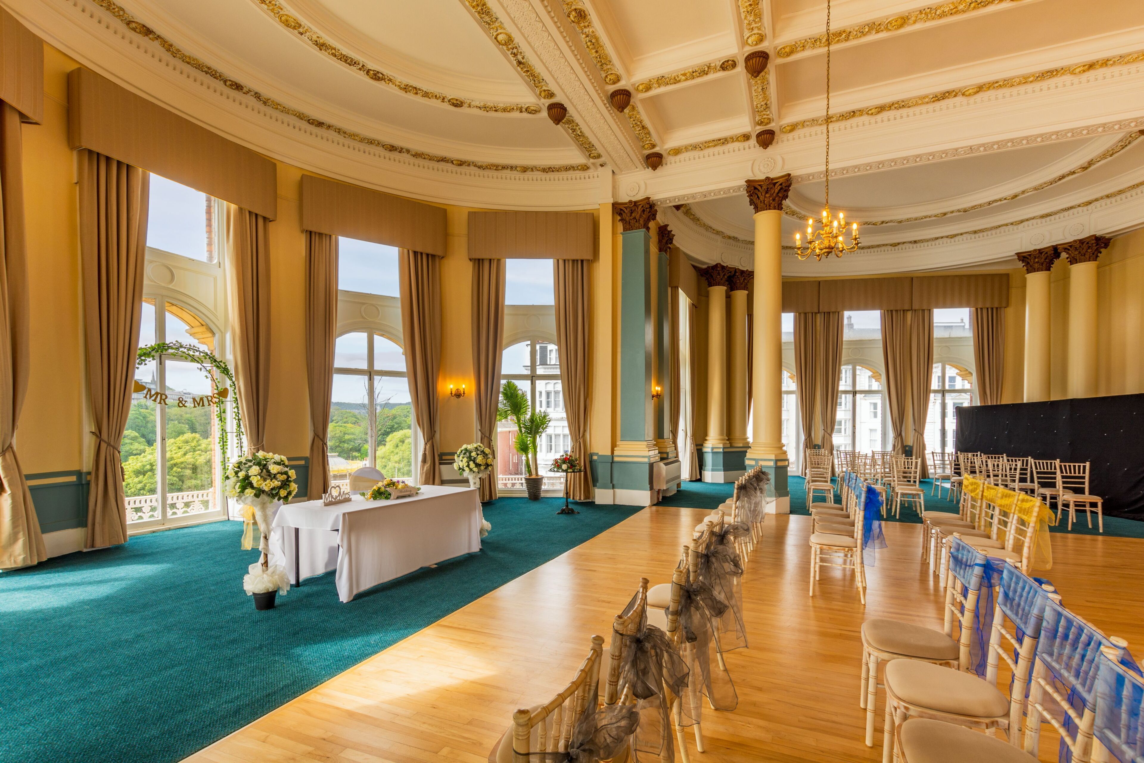 A grand hall with a long table, chairs, and a stage.