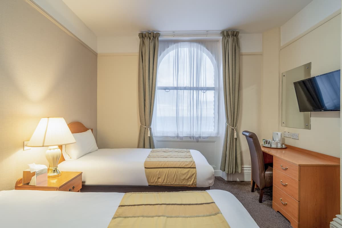 Une chambre d’hôtel avec deux lits, un bureau avec une chaise, une télévision et une fenêtre avec des rideaux.