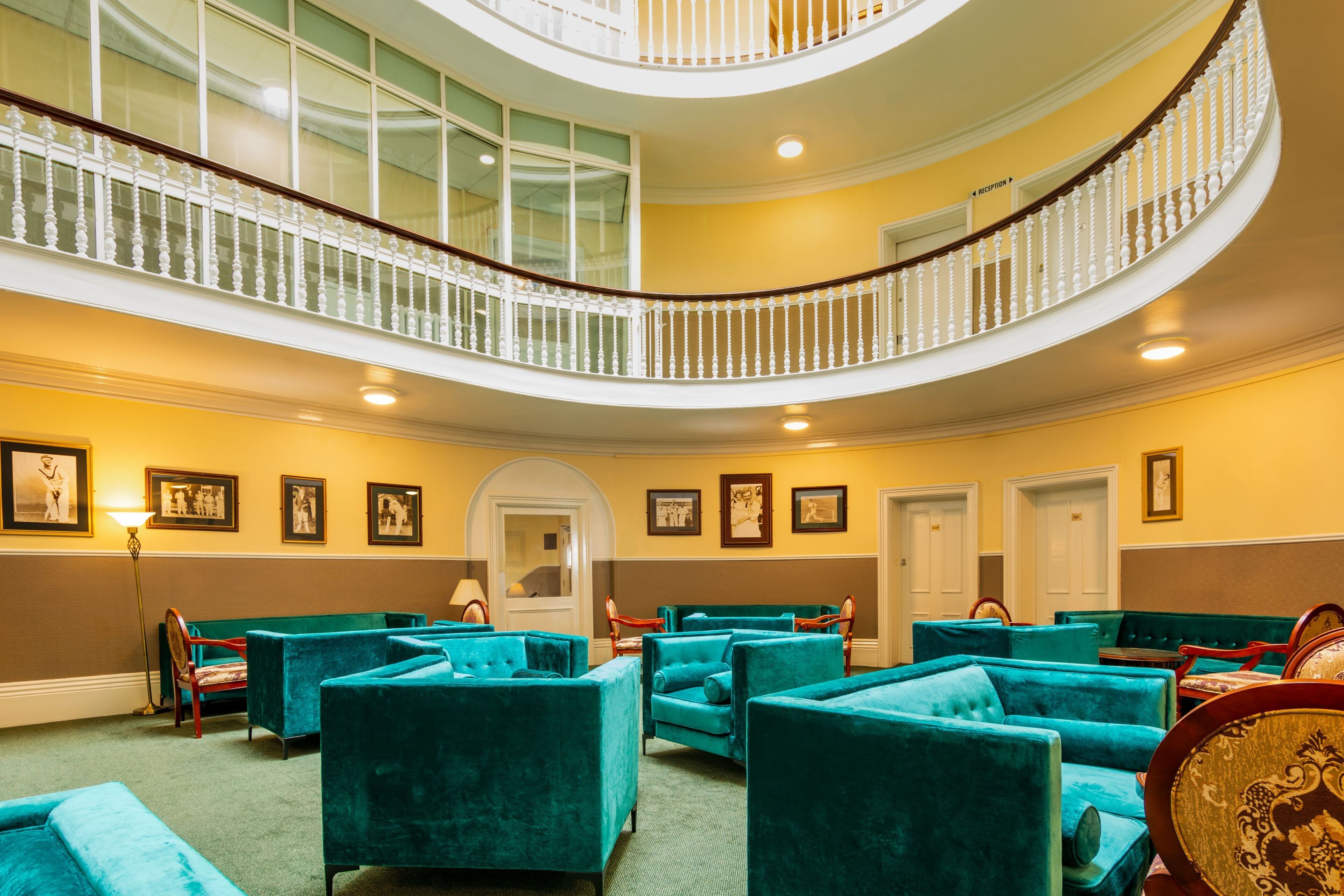 Un hall d’hôtel avec un escalier à volutes, des sièges recouverts d’un tissu turquoise, des tableaux encadrés accrochés aux murs et un comptoir de réception.