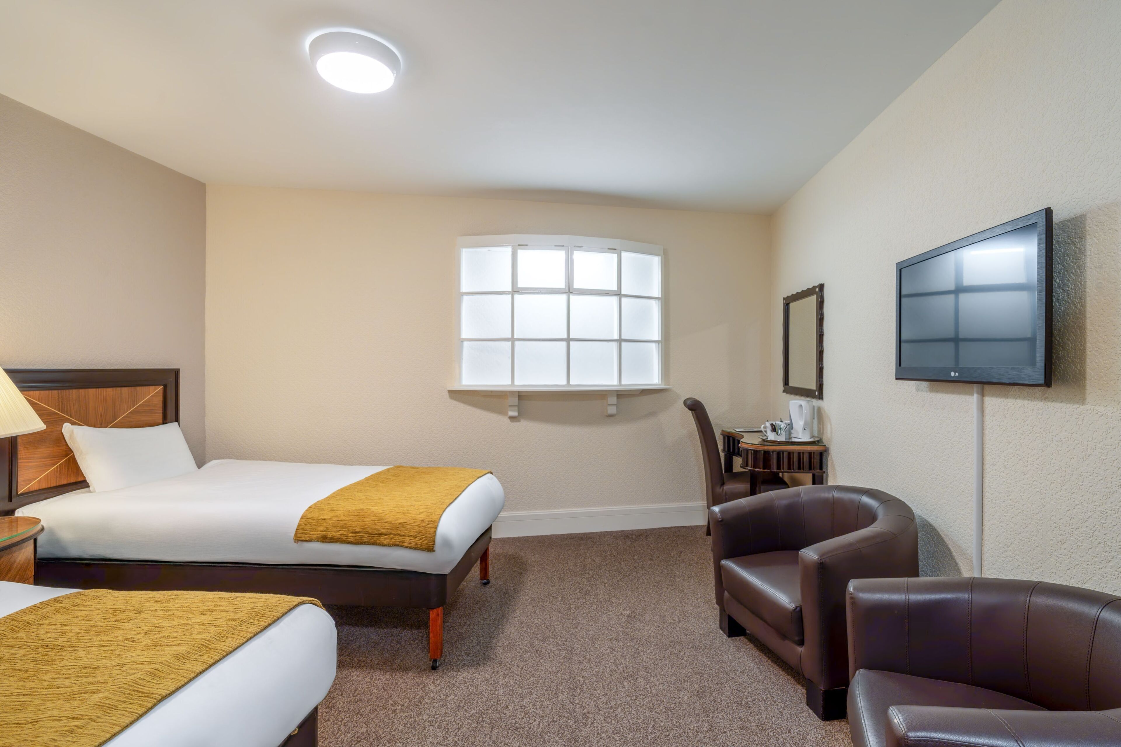 A hotel room with two beds, a TV, a window, and a seating area.