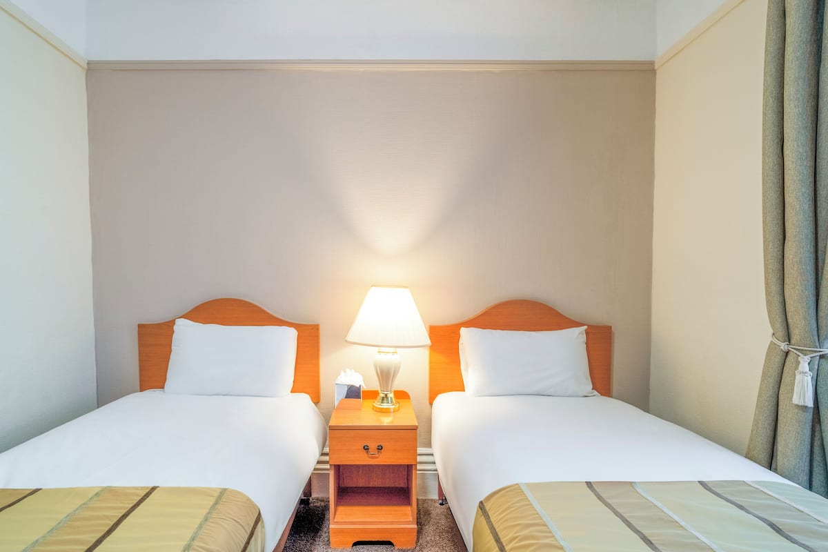 Une chambre d’hôtel avec deux lits, une table de chevet avec une lampe et un rideau.