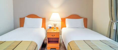 A hotel room with two beds, a nightstand with a lamp, and a curtain.
