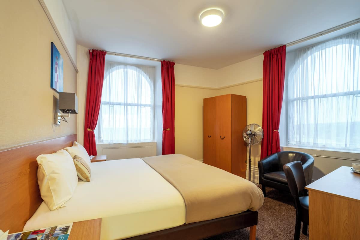 Une chambre d’hôtel comprenant un lit, un bureau, une chaise, une armoire et une lampe sur pied.