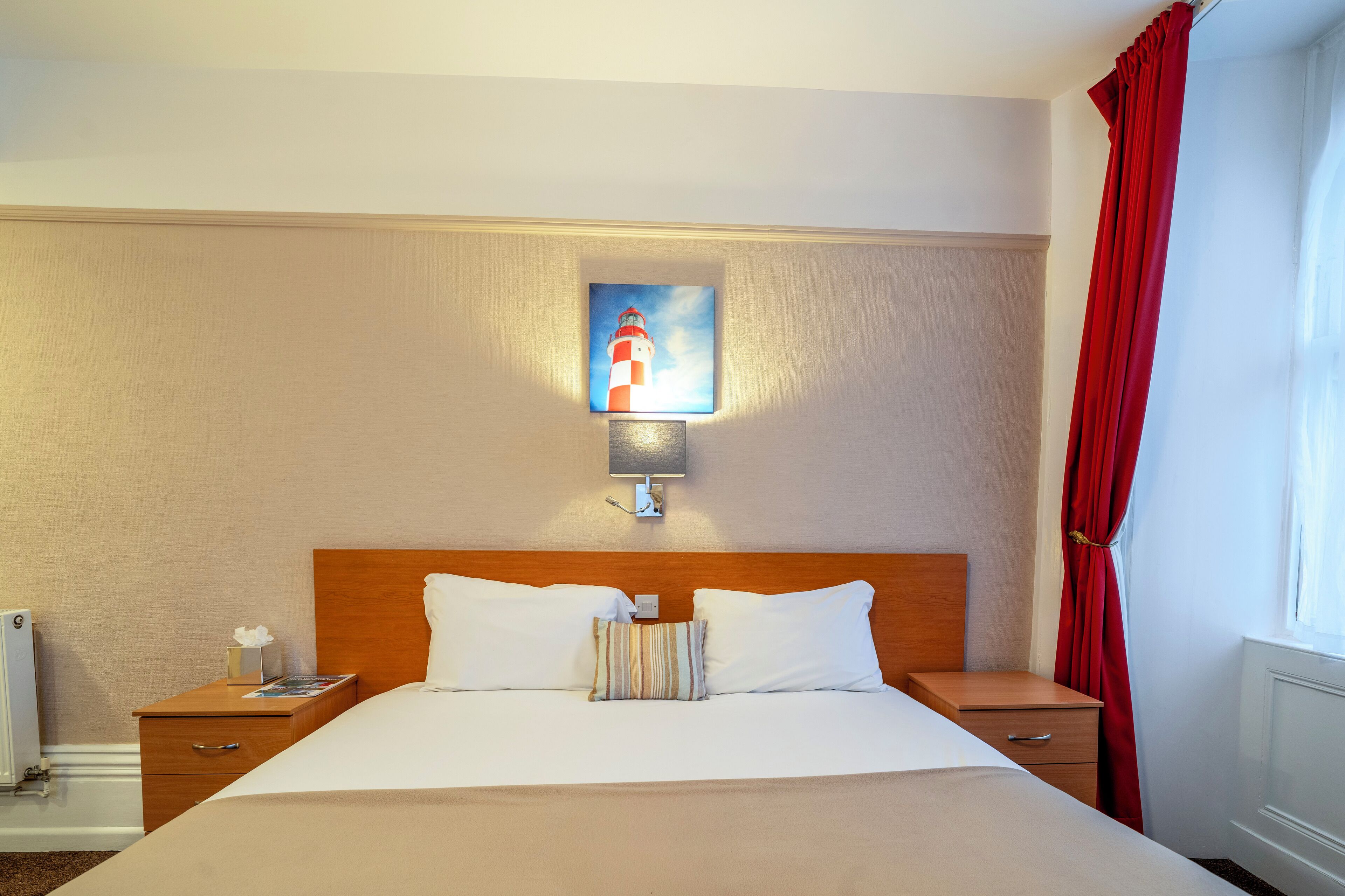 Une chambre d’hôtel avec un grand lit, une table de chevet, une lampe et un tableau représentant un phare accroché au mur.