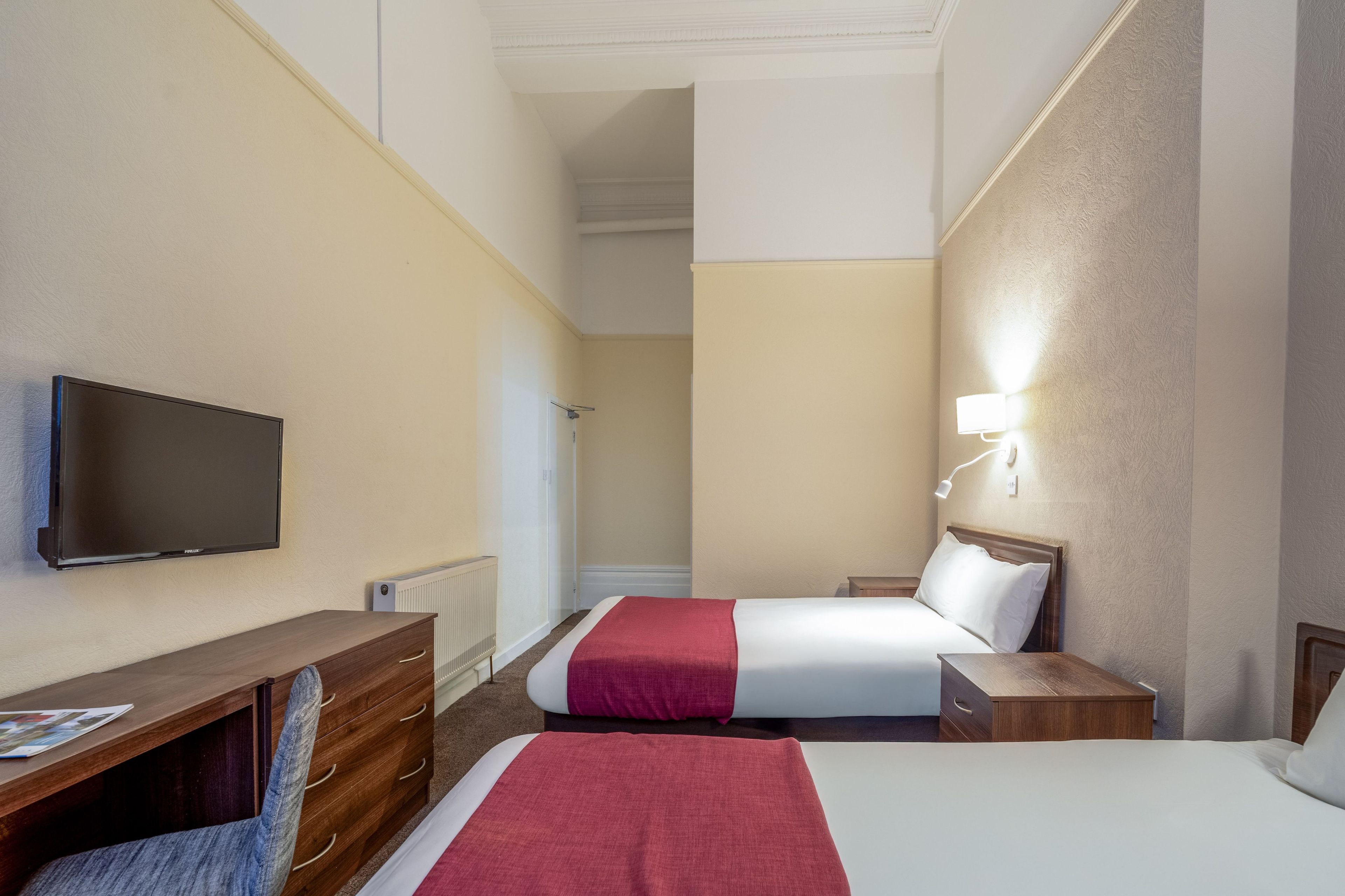 Une chambre d’hôtel équipée d’un lit, d’un bureau, d’une télévision et d’une lampe fixée au mur.