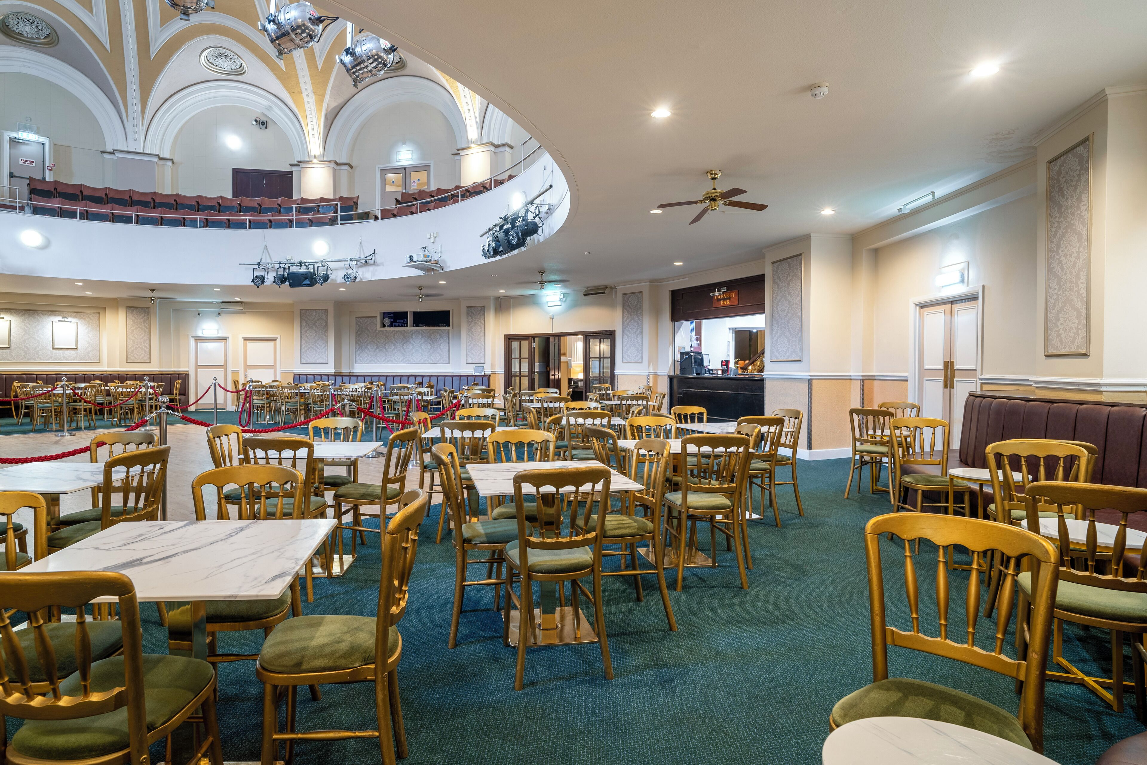 A spacious dining area with multiple tables and chairs, a balcony with seating, and a stage for performances.