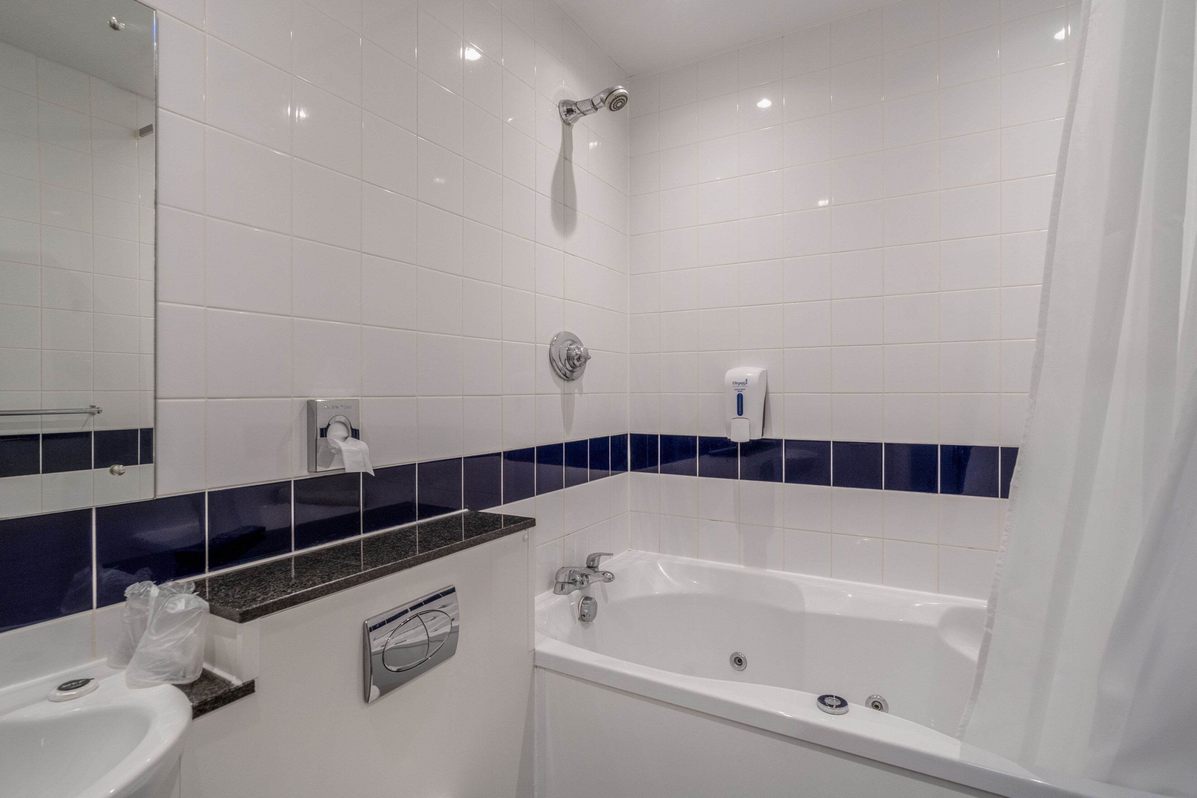A modern bathroom with a bathtub, a sink, a mirror, and a towel dispenser.
