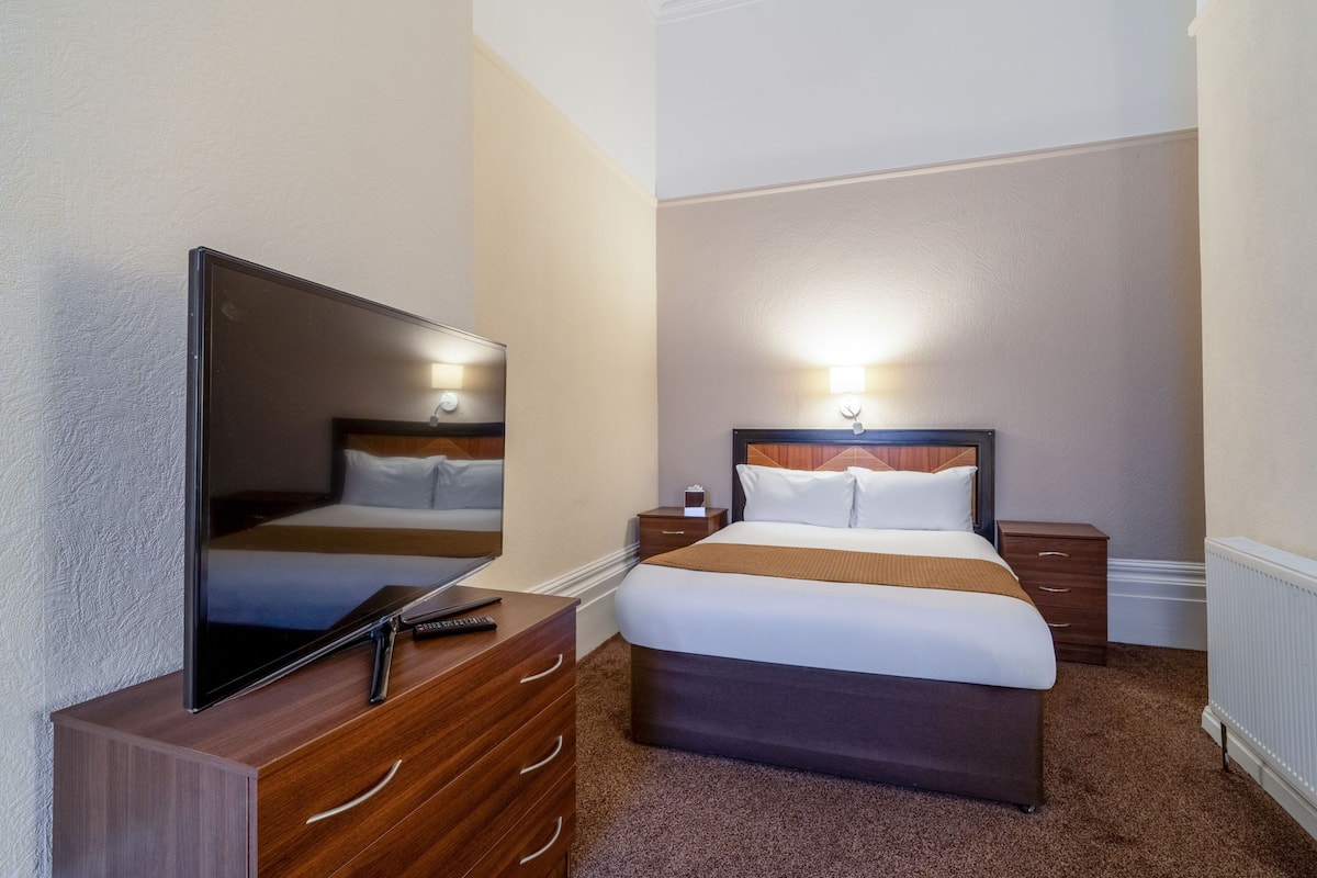 Une chambre d’hôtel avec un lit, une télévision, une commode et une table de chevet.