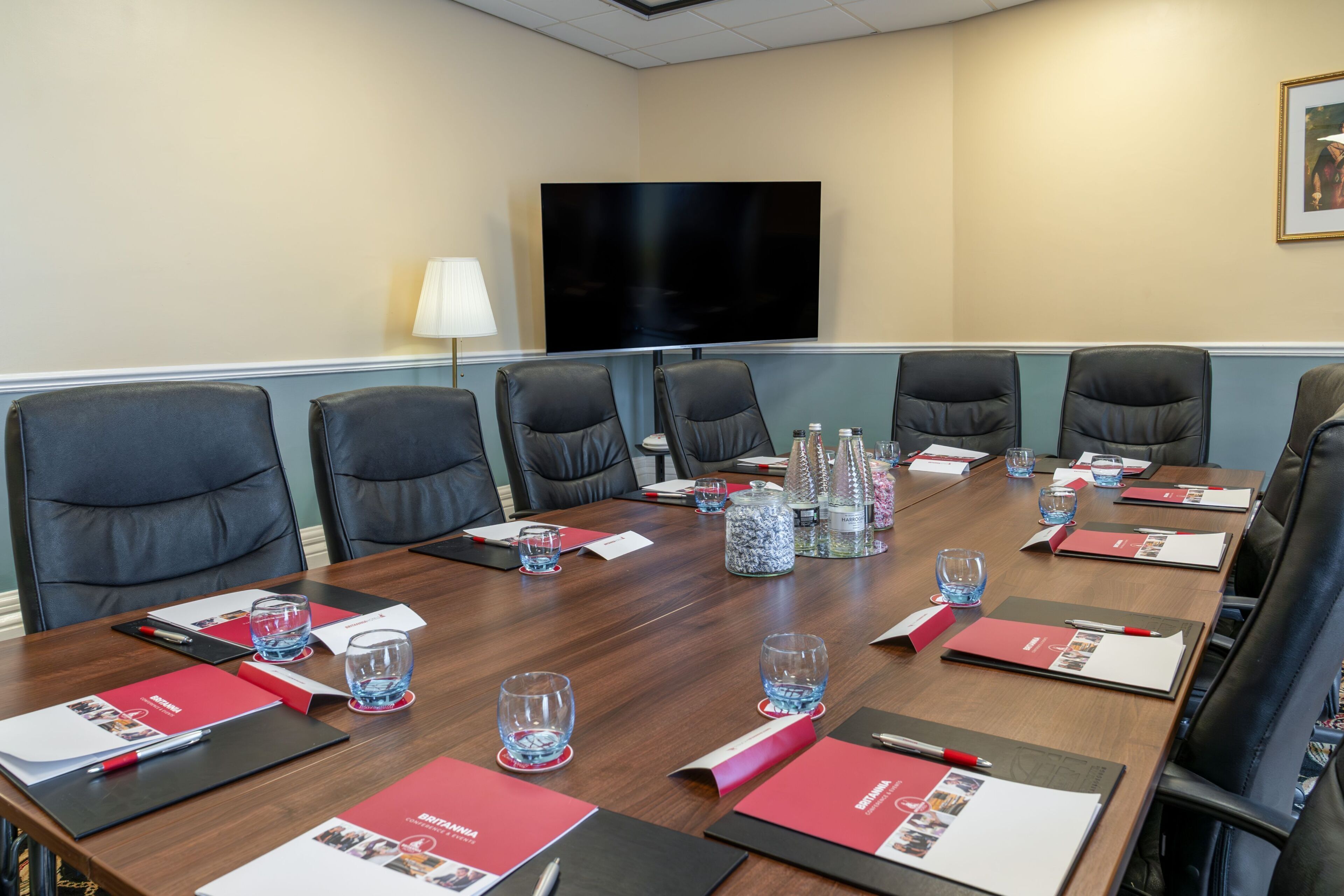 Une salle de conférence équipée d’une grande table, de chaises, d’un téléviseur et de divers accessoires, comme des bouteilles d’eau et des classeurs.