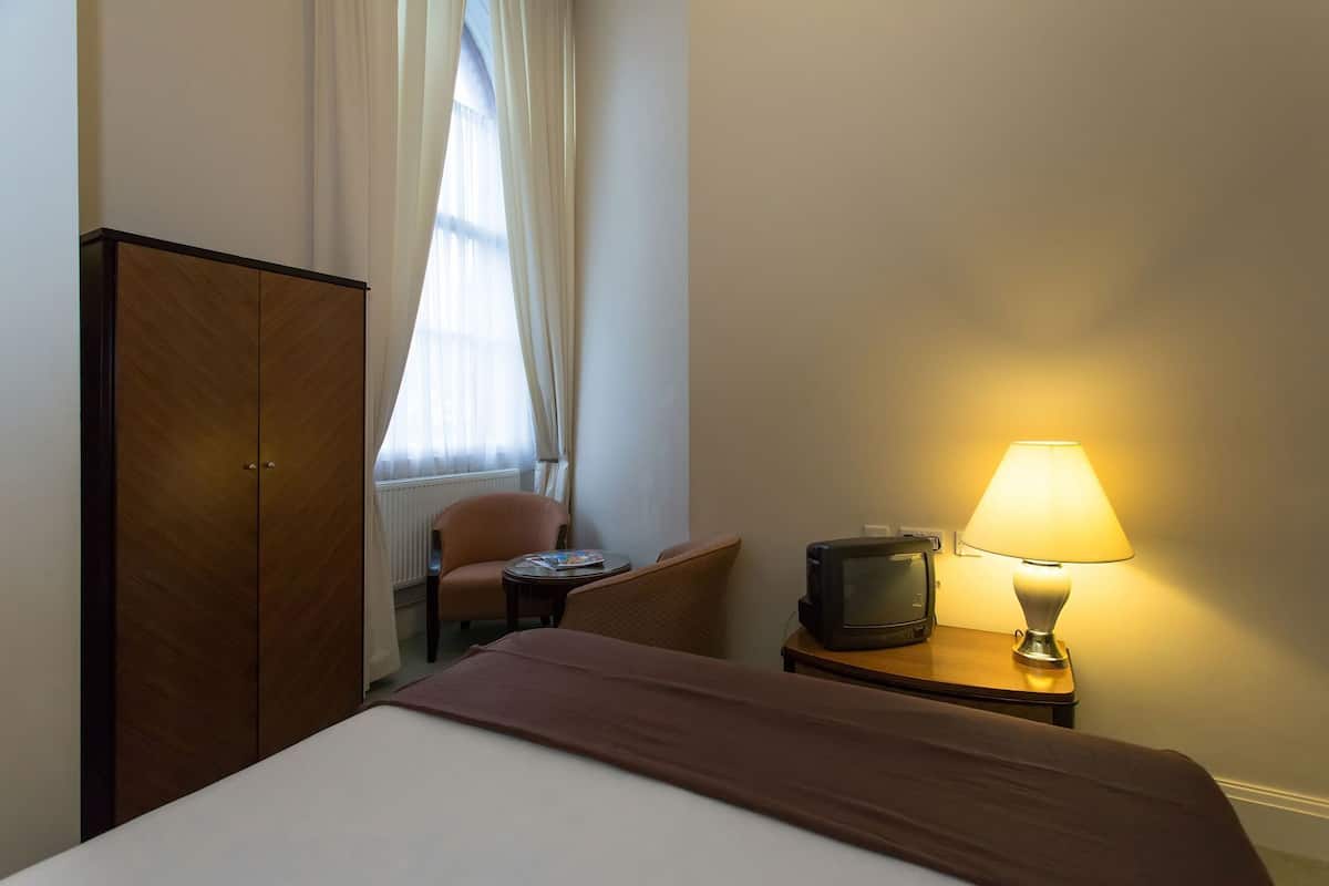 Une chambre d’hôtel comprenant un lit, une télévision, une lampe, une chaise et une armoire.