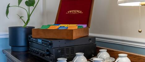 A wooden box with a red interior labeled "TWININGS" containing colorful items, placed on a table with a potted plant and audio equipment.