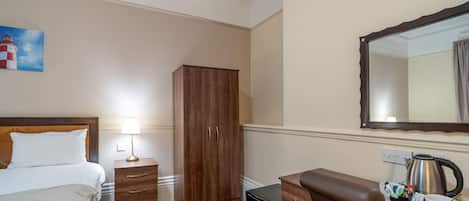 Habitación de hotel con cama, armario de madera, escritorio con tetera y bandeja, y una pintura de un faro.