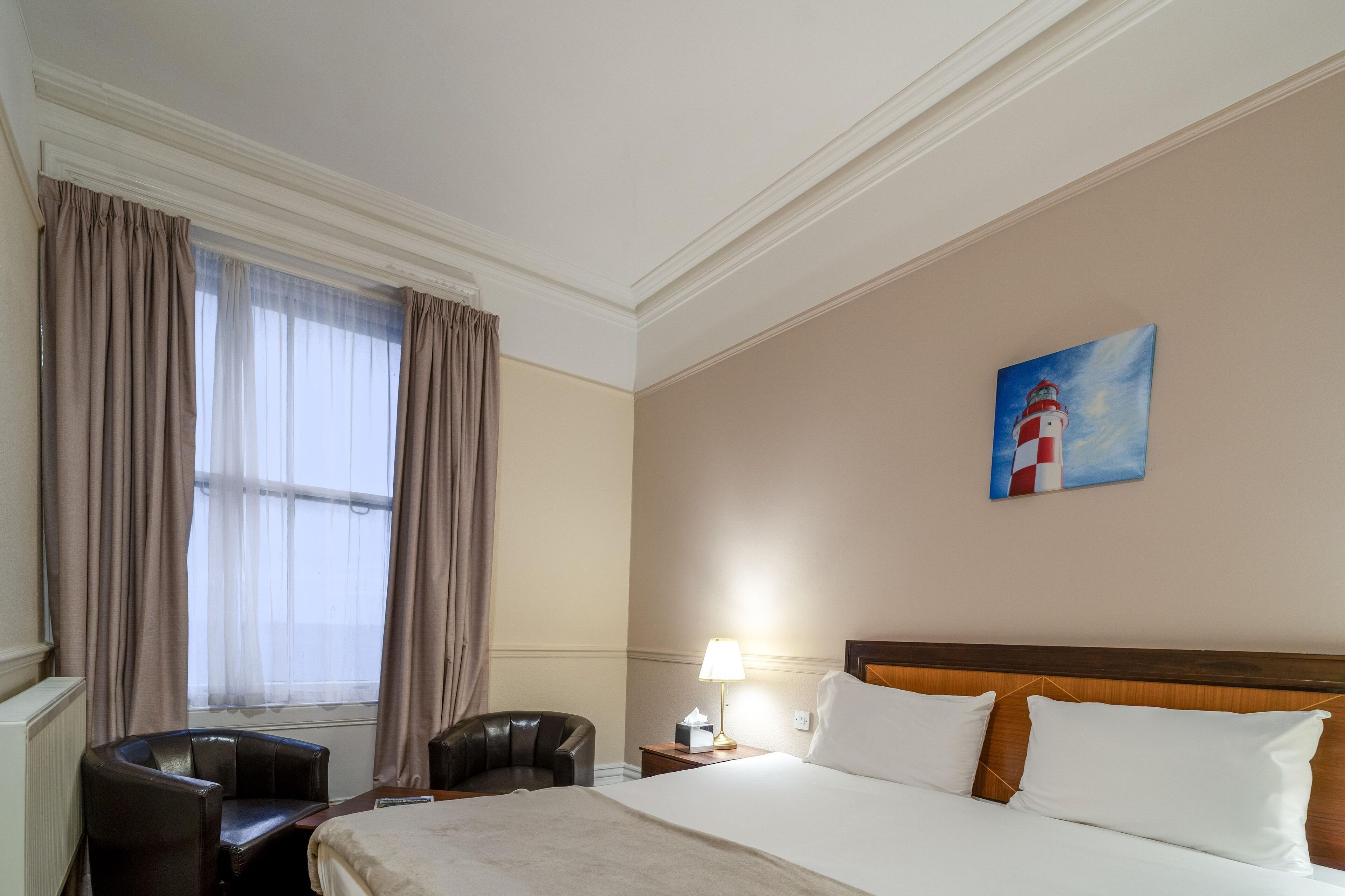 Une chambre d’hôtel avec un lit, un bureau, une chaise, une table de chevet avec une lampe et un tableau au mur.