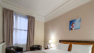 Ein Hotelzimmer mit Bett, Schreibtisch, Stuhl, Nachttisch mit Lampe und einem Bild an der Wand.