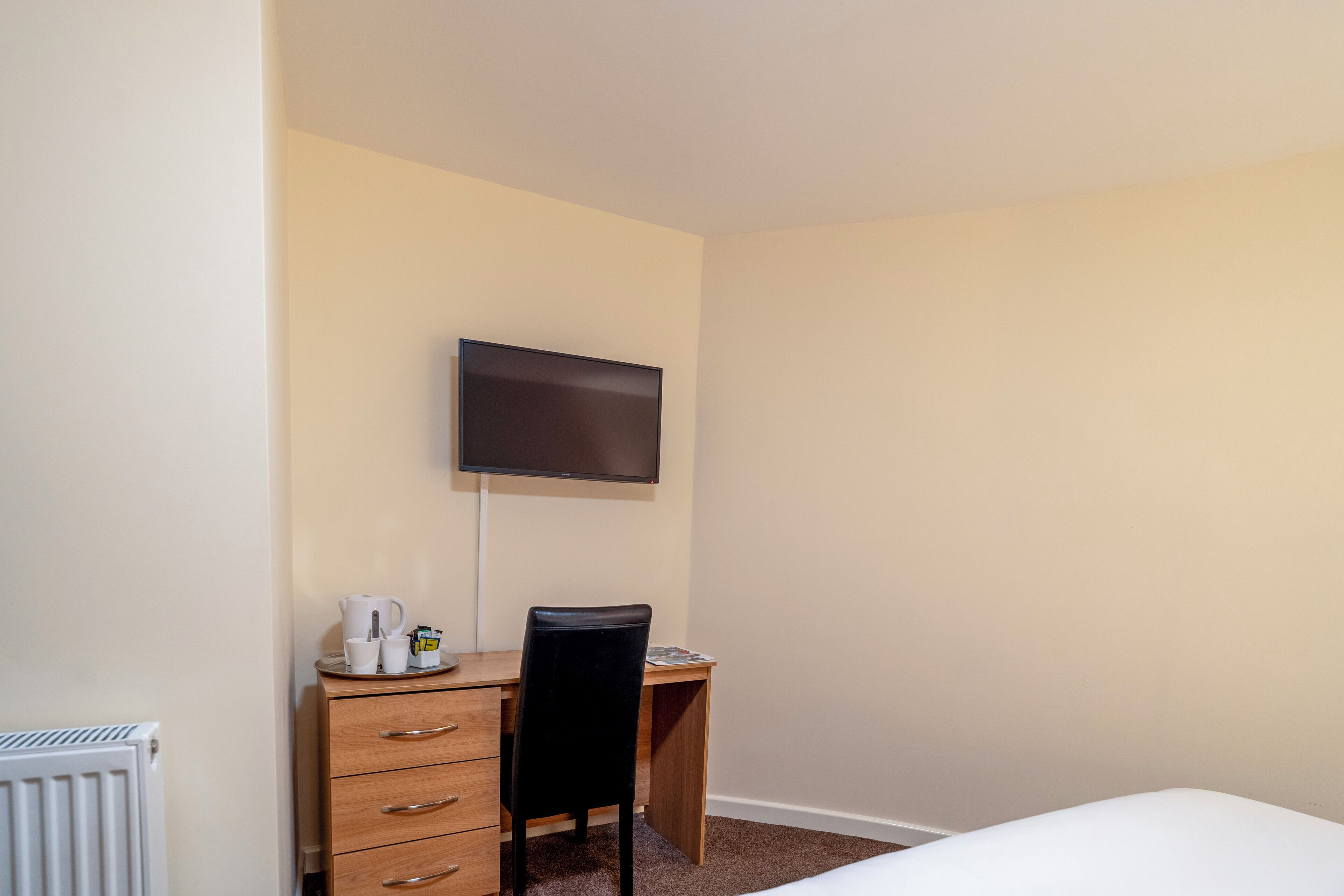Una habitación de hotel con cama, escritorio con silla, televisor en la pared y radiador.