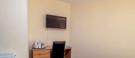 Una habitación de hotel con cama, escritorio con silla, televisor en la pared y radiador.