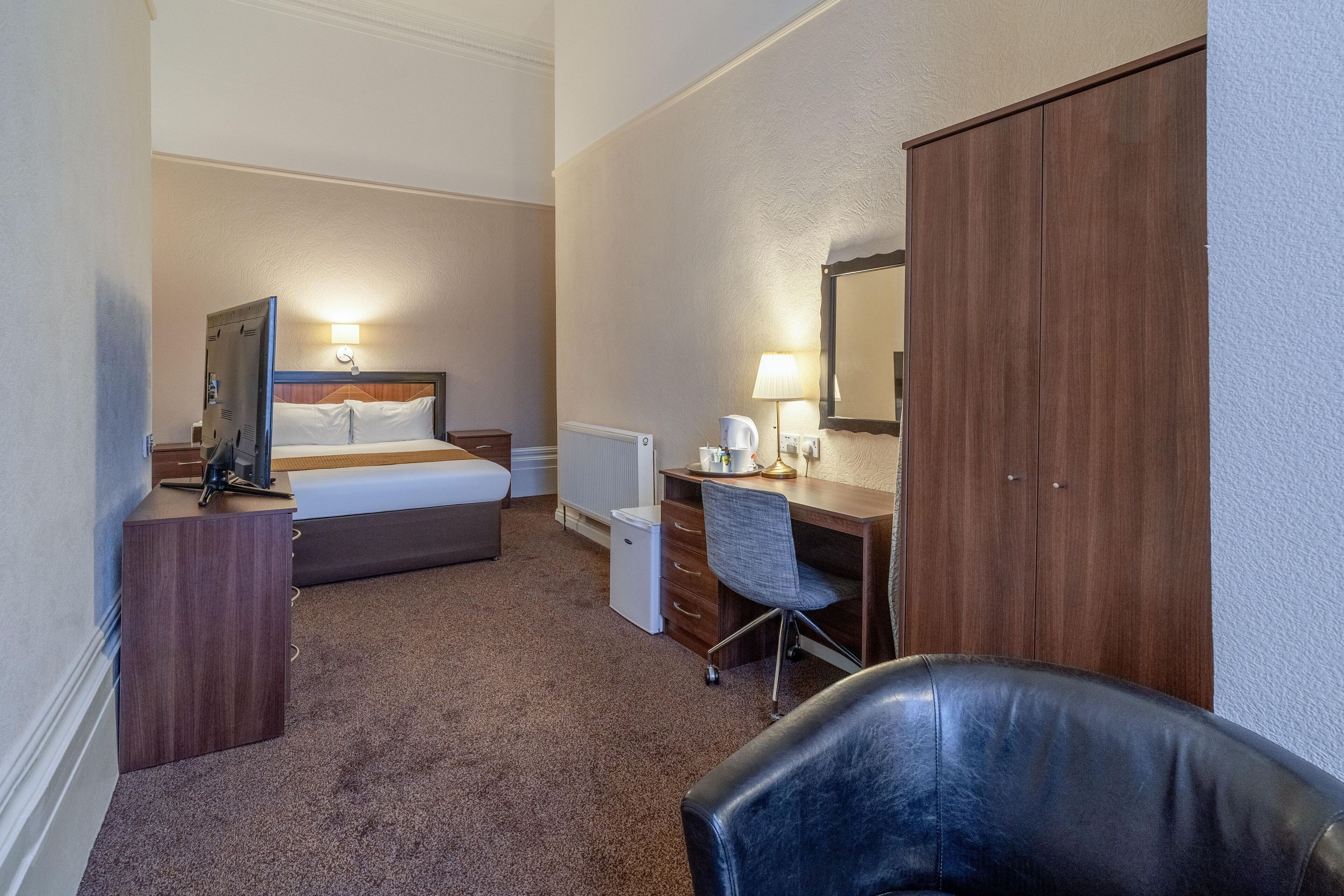 Een hotelkamer met een bed, een bureau met stoel, een kledingkast en een spiegel.