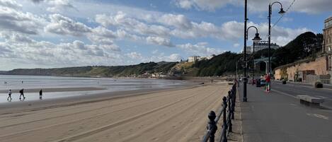 A beach with a promenade, a bridge in the background, and buildings on the hillside.