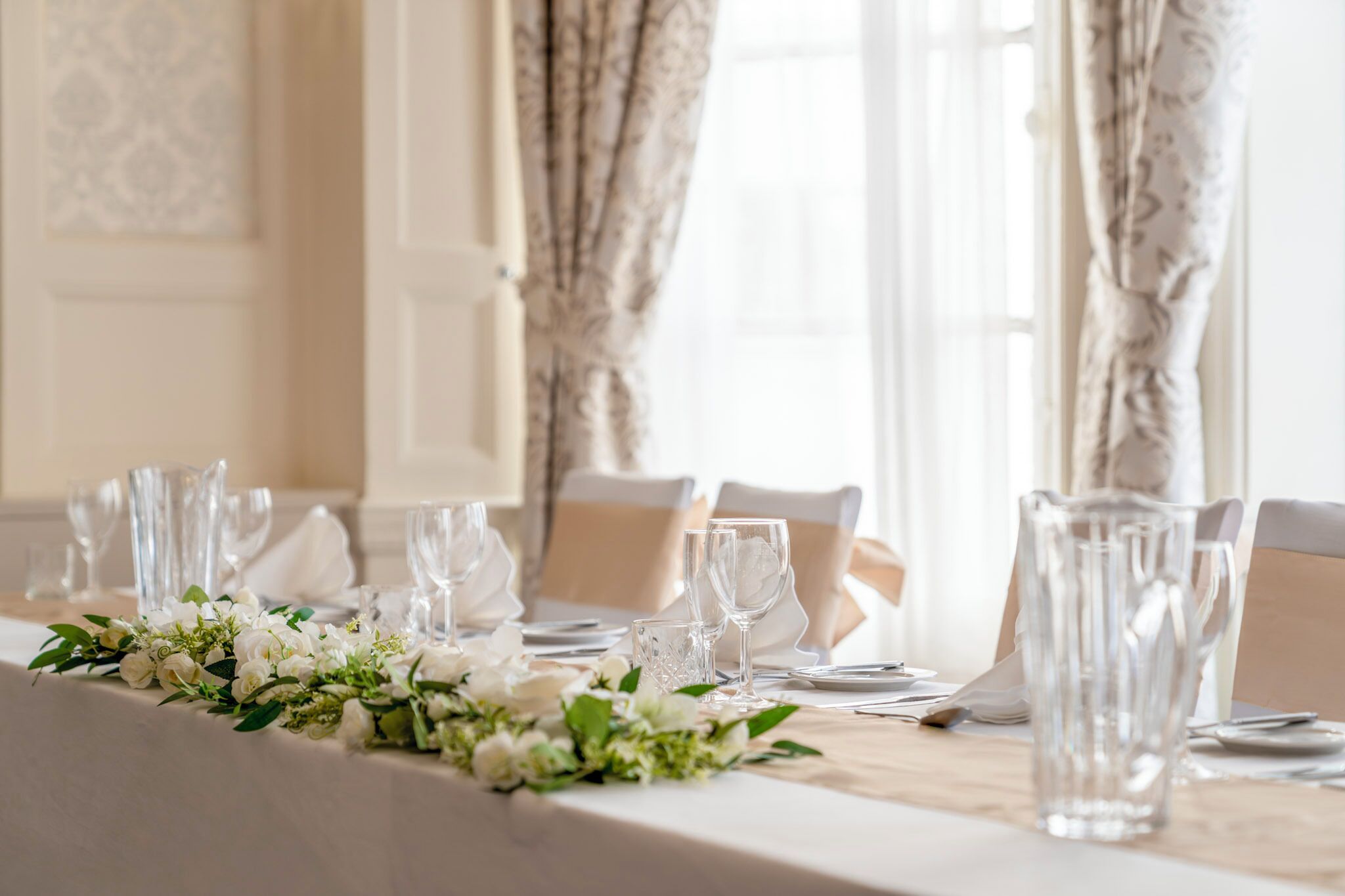 A dining table set with clear glassware, white tablecloth, and a floral centerpiece.