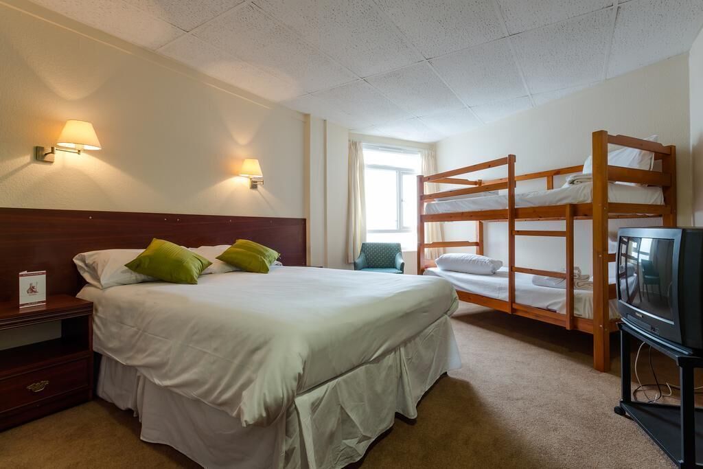 A hotel room with a single bed, two wall-mounted lamps, a TV, bunk beds, and a window.