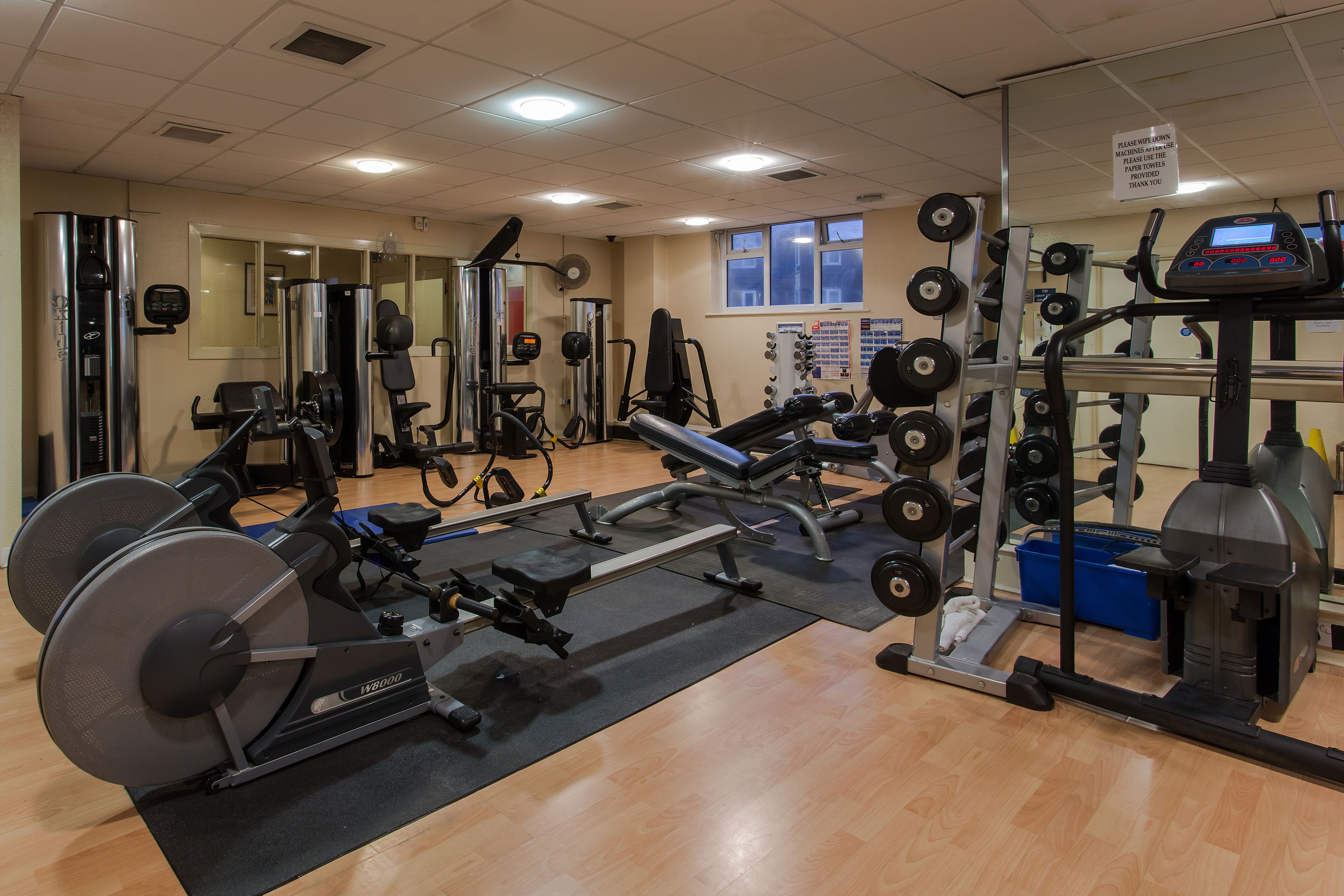 A gym with various exercise equipment, including a rowing machine, weight bench, and dumbbells.