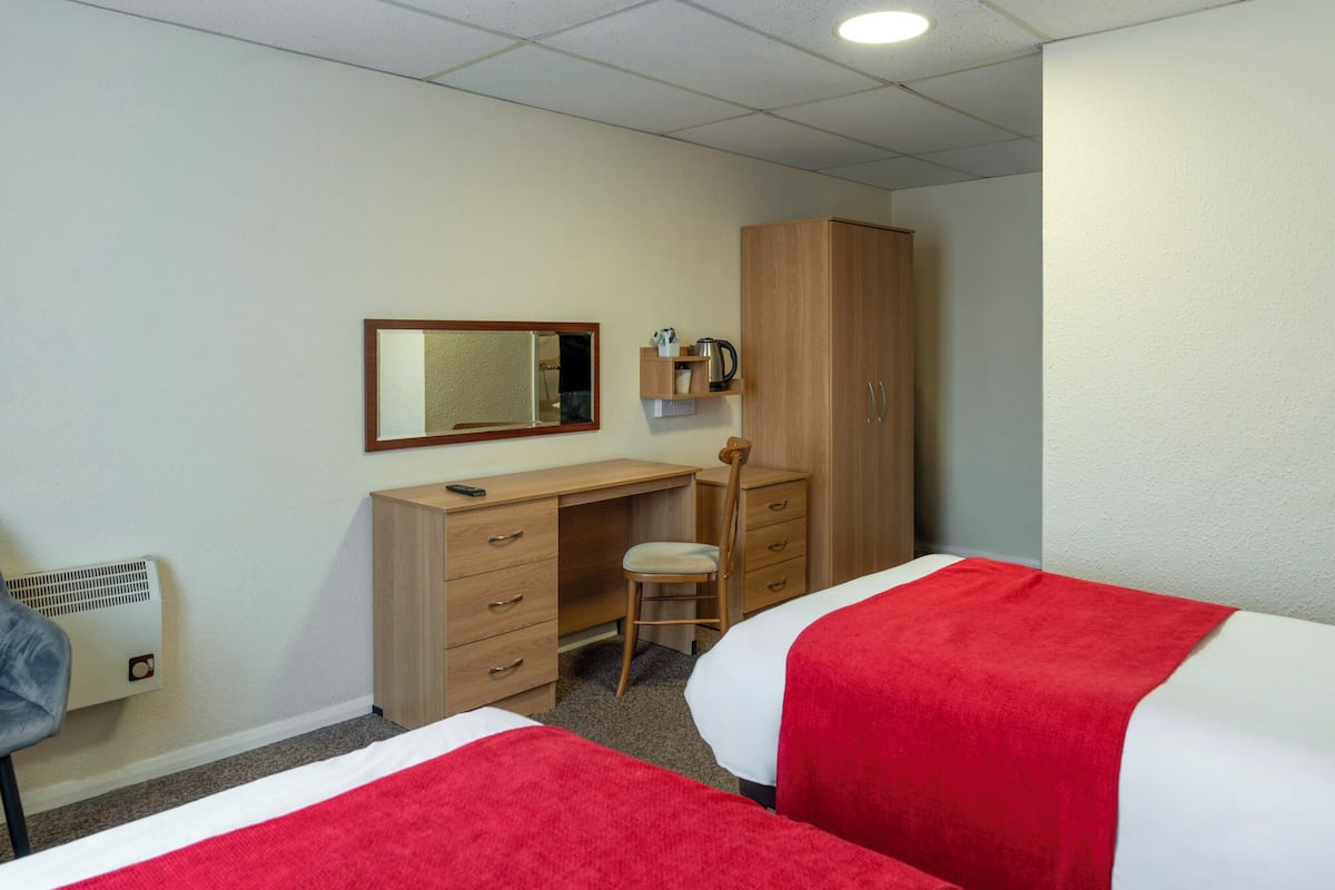 Une chambre d’hôtel avec deux lits, un bureau, une chaise, une armoire, un miroir et un radiateur.