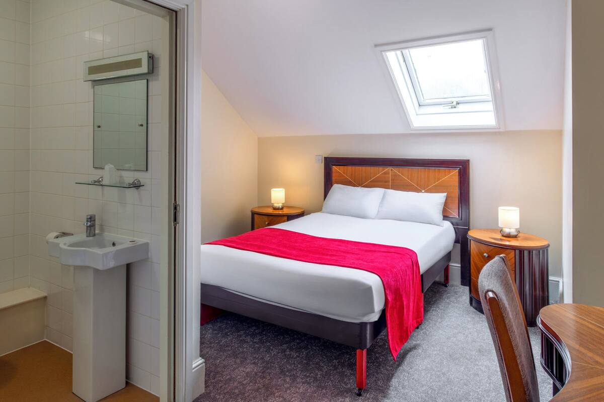 Une chambre d’hôtel avec un lit, des tables de chevet, une fenêtre, un miroir et un lavabo.