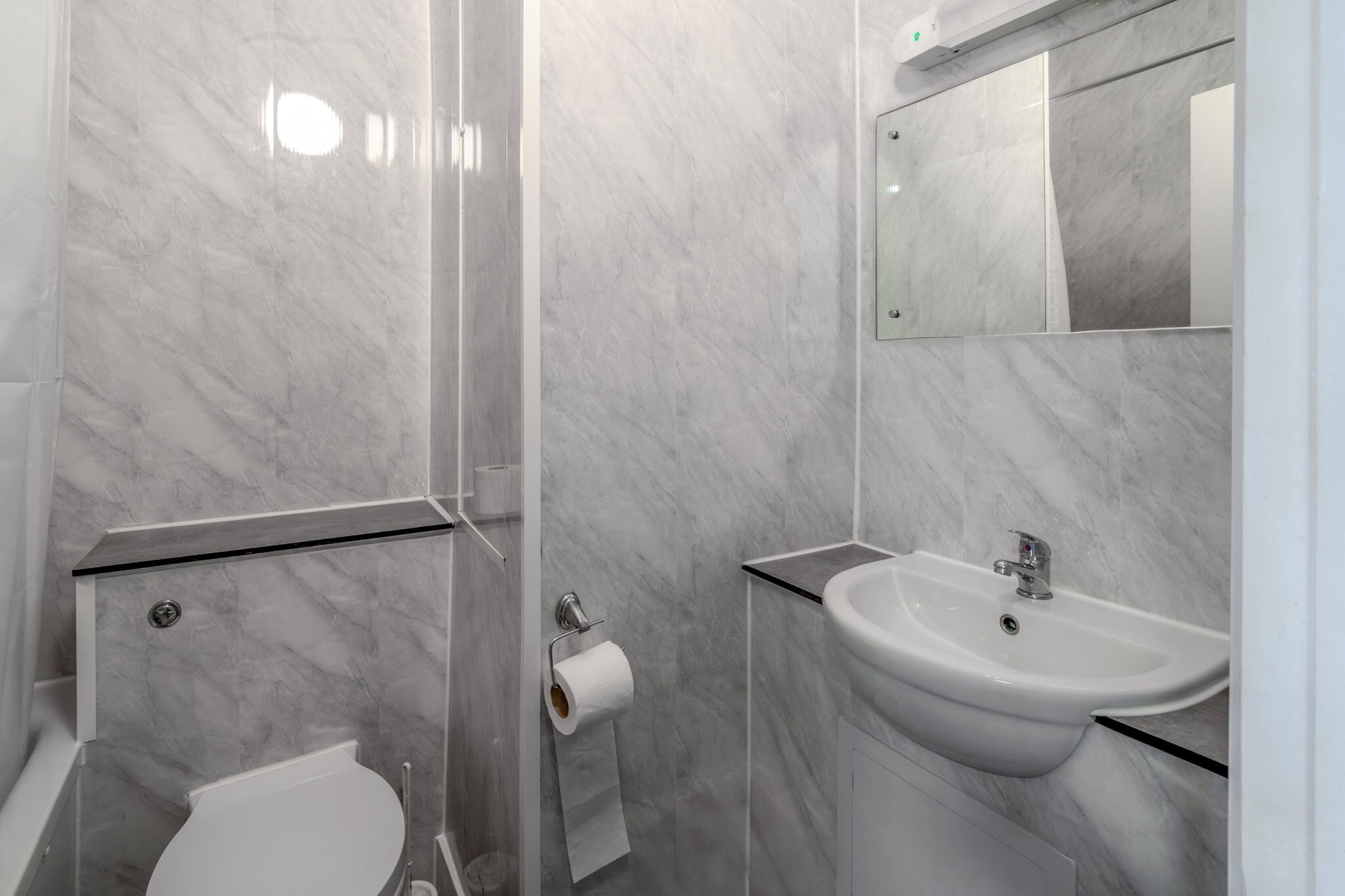 A modern bathroom with a toilet, a glass shower enclosure, a sink, and a mirror.