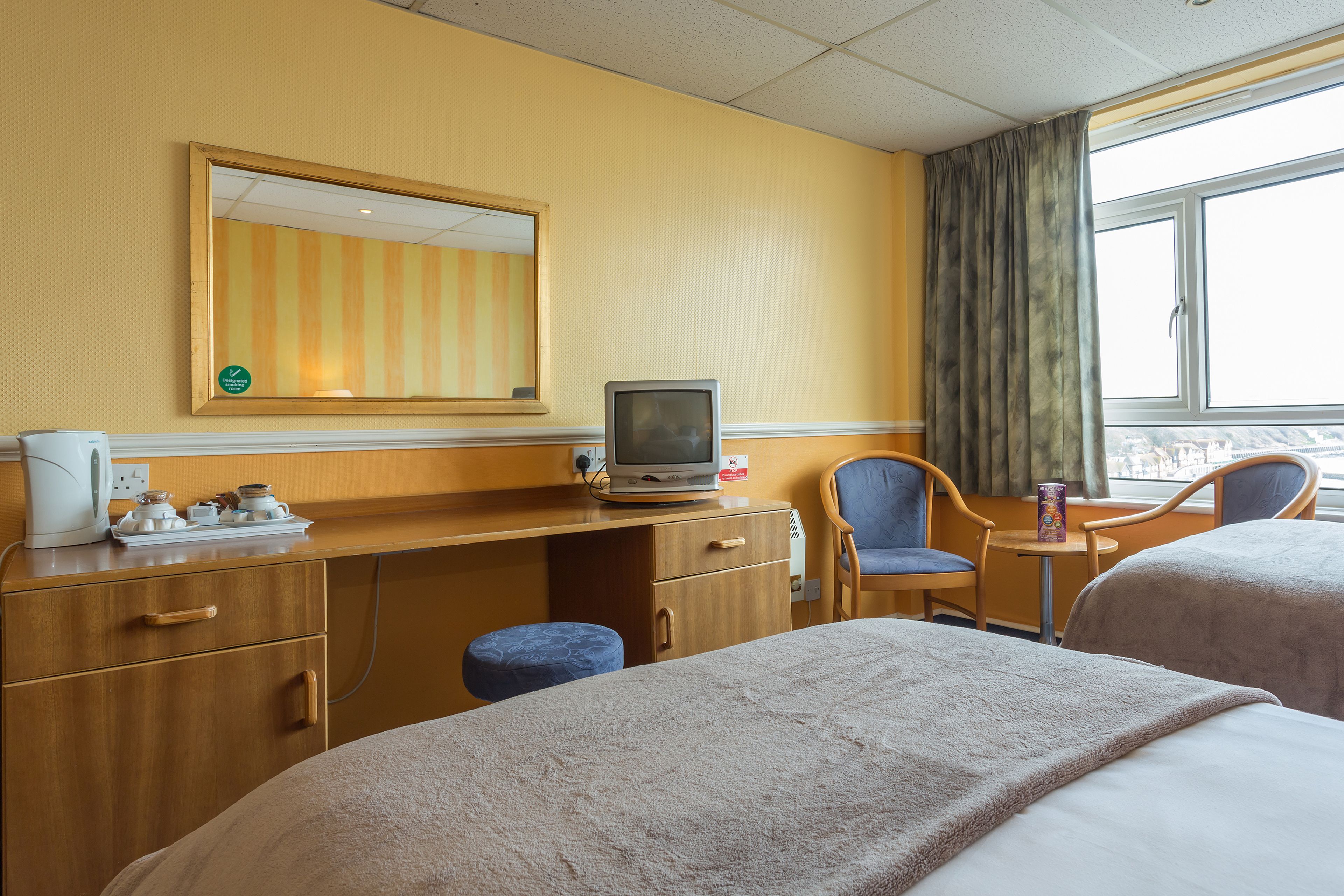 A hotel room with two beds, a desk with a television, a chair, and a window with curtains.