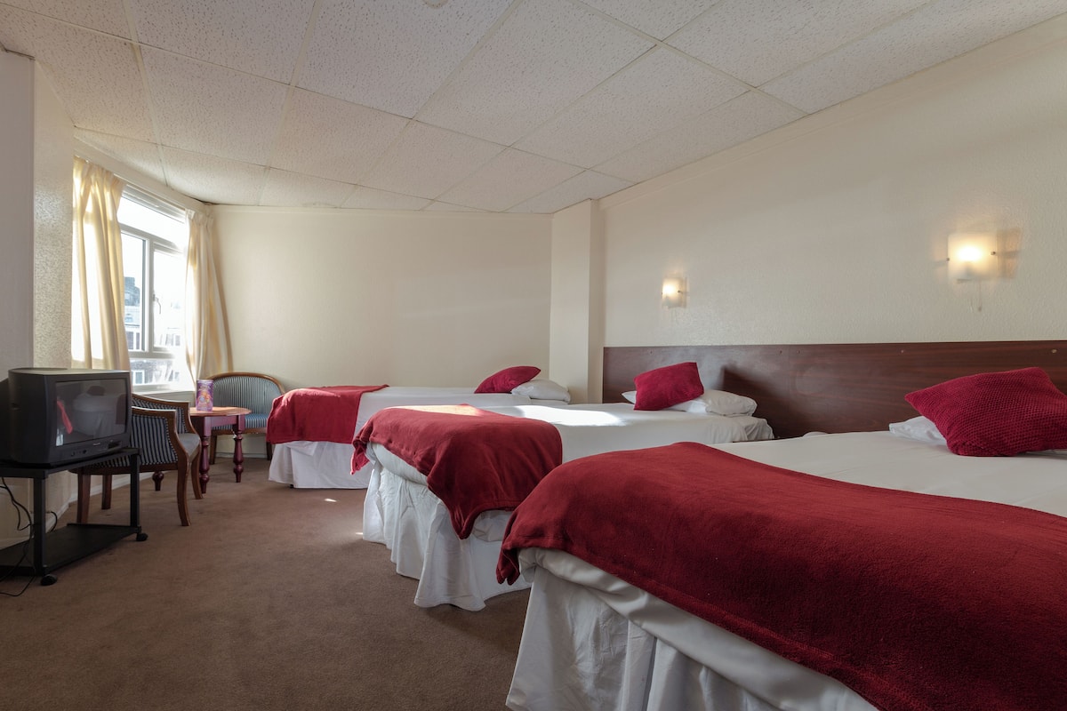 Une chambre d’hôtel avec trois lits, une télévision, un bureau et une chaise.