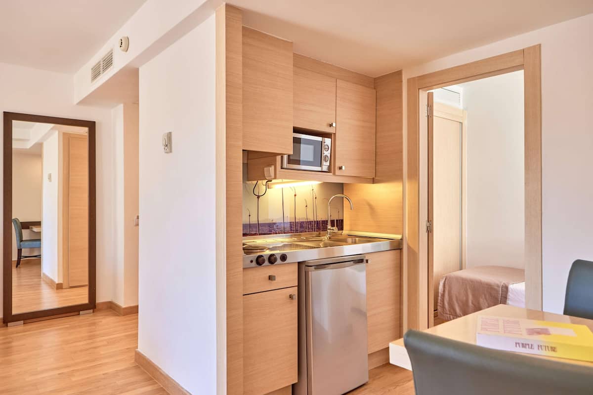 A compact kitchen with a microwave, stove, and refrigerator, wooden cabinets, and a dining area with a table and chair.