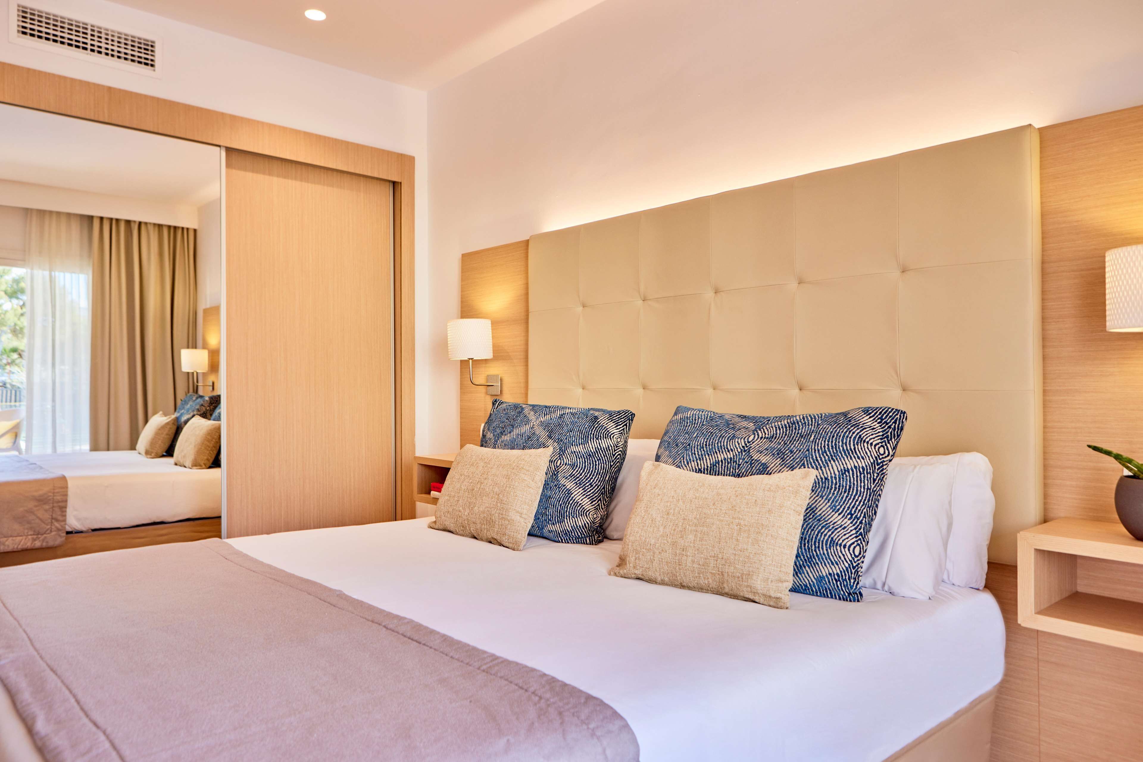 Une chambre d’hôtel avec un grand lit, une tête de lit en bois et une table de chevet avec une lampe.
