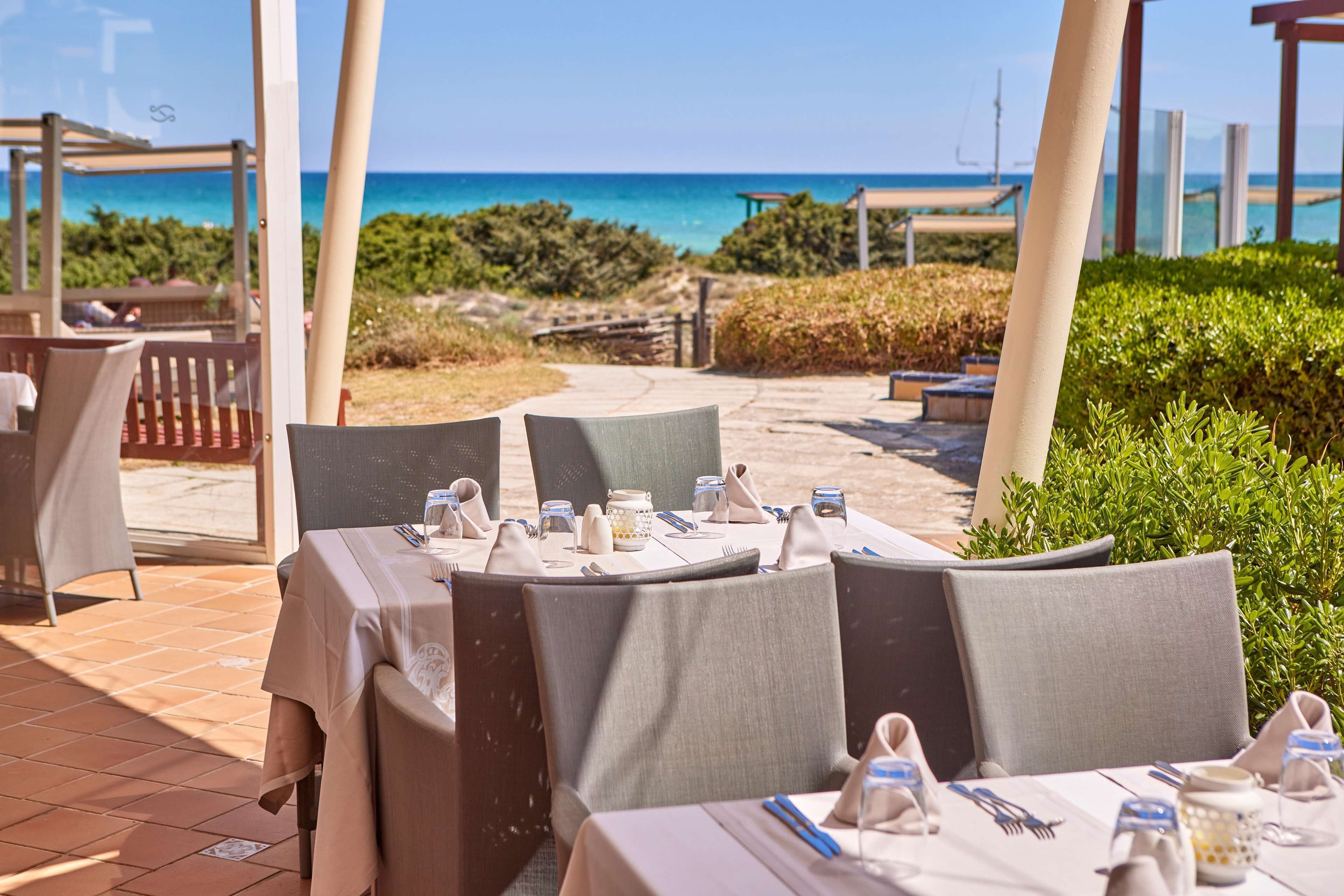 Un restaurant en bord de mer, avec des tables dressées pour le dîner, offrant une vue sur l’océan.