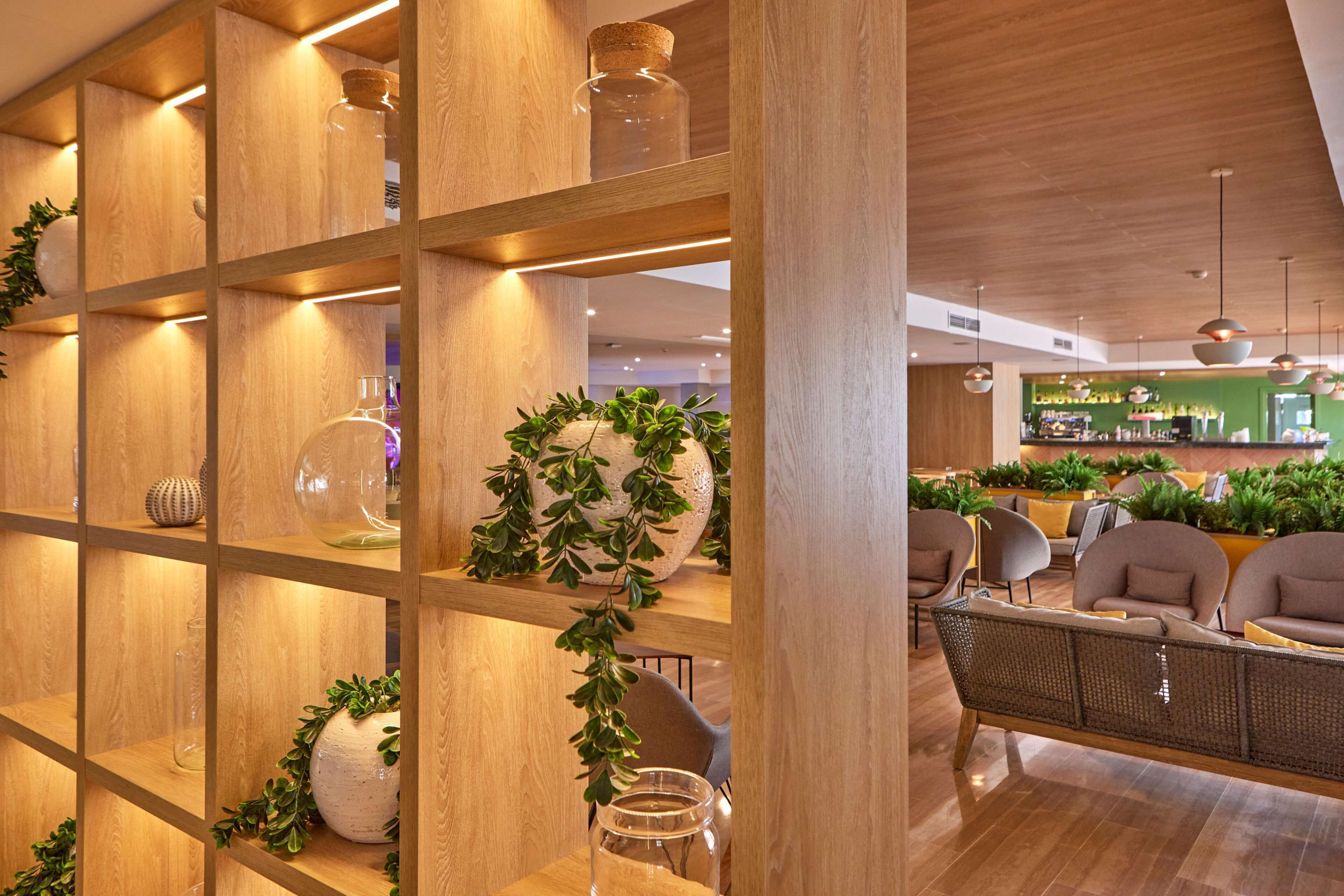 Ein modernes Interieur mit Holzböden, die Glasbehälter und Vasen zeigen, eine Sitzecke mit Sofas und eine Bar im Hintergrund.