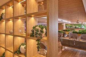 Un interior moderno con estanterías de madera que exhiben frascos y jarrones de vidrio, una zona de estar con sofás y un bar al fondo.
