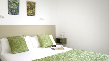 Una cama bien hecha con ropa de cama verde, una mesita de noche con un libro y dos cuadros en la pared.