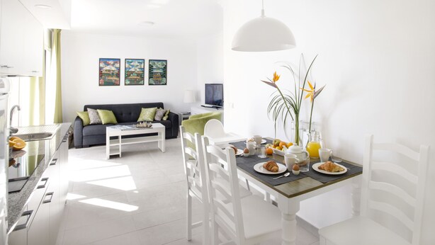 A modern living room with a dining area, white furniture, and artwork on the walls. - El Guarapo Apartamentos (Teguise)