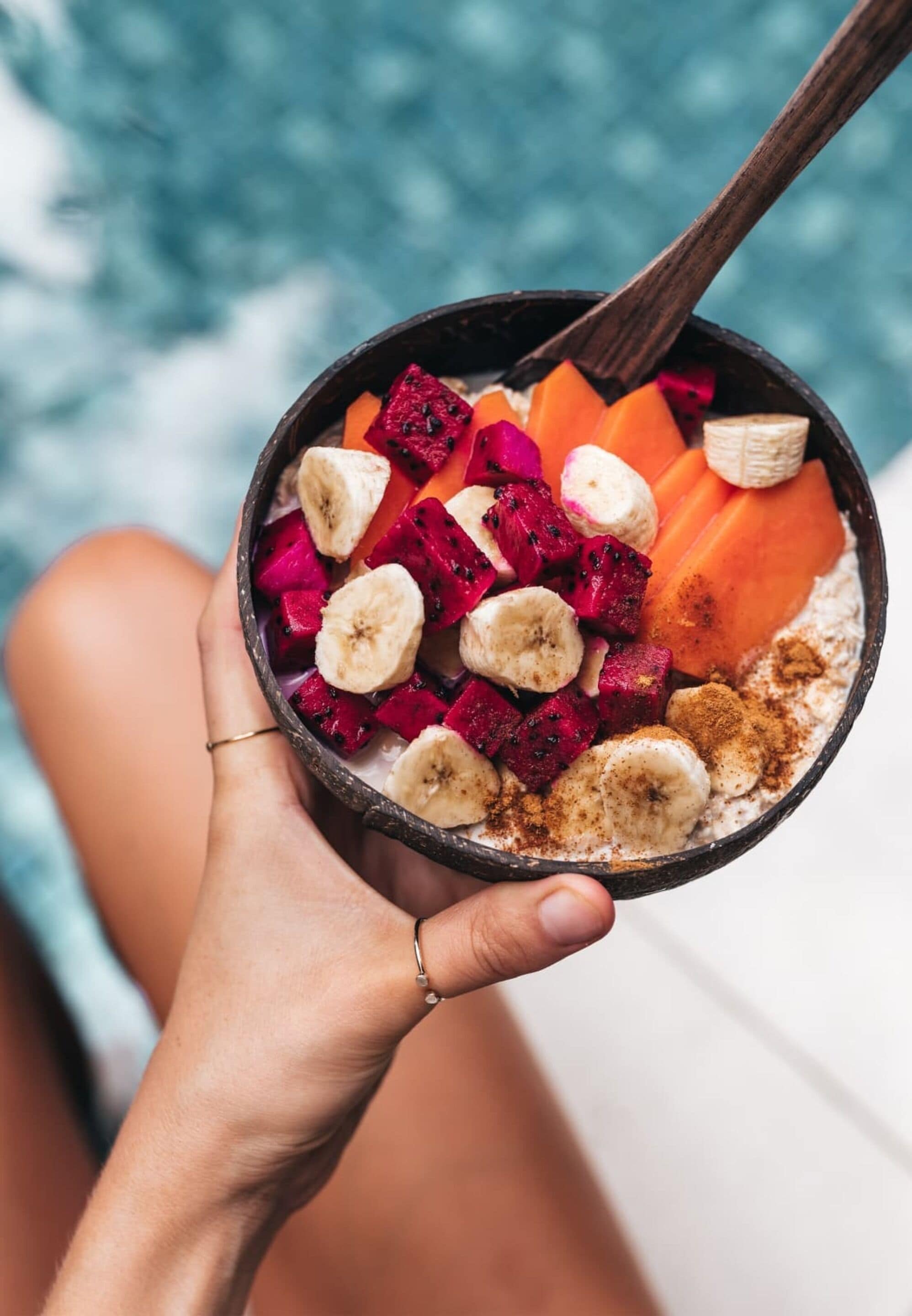 A person holding a bowl with a variety of fruits and a spoon.