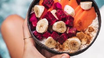 A person holding a bowl with a variety of fruits and a spoon.