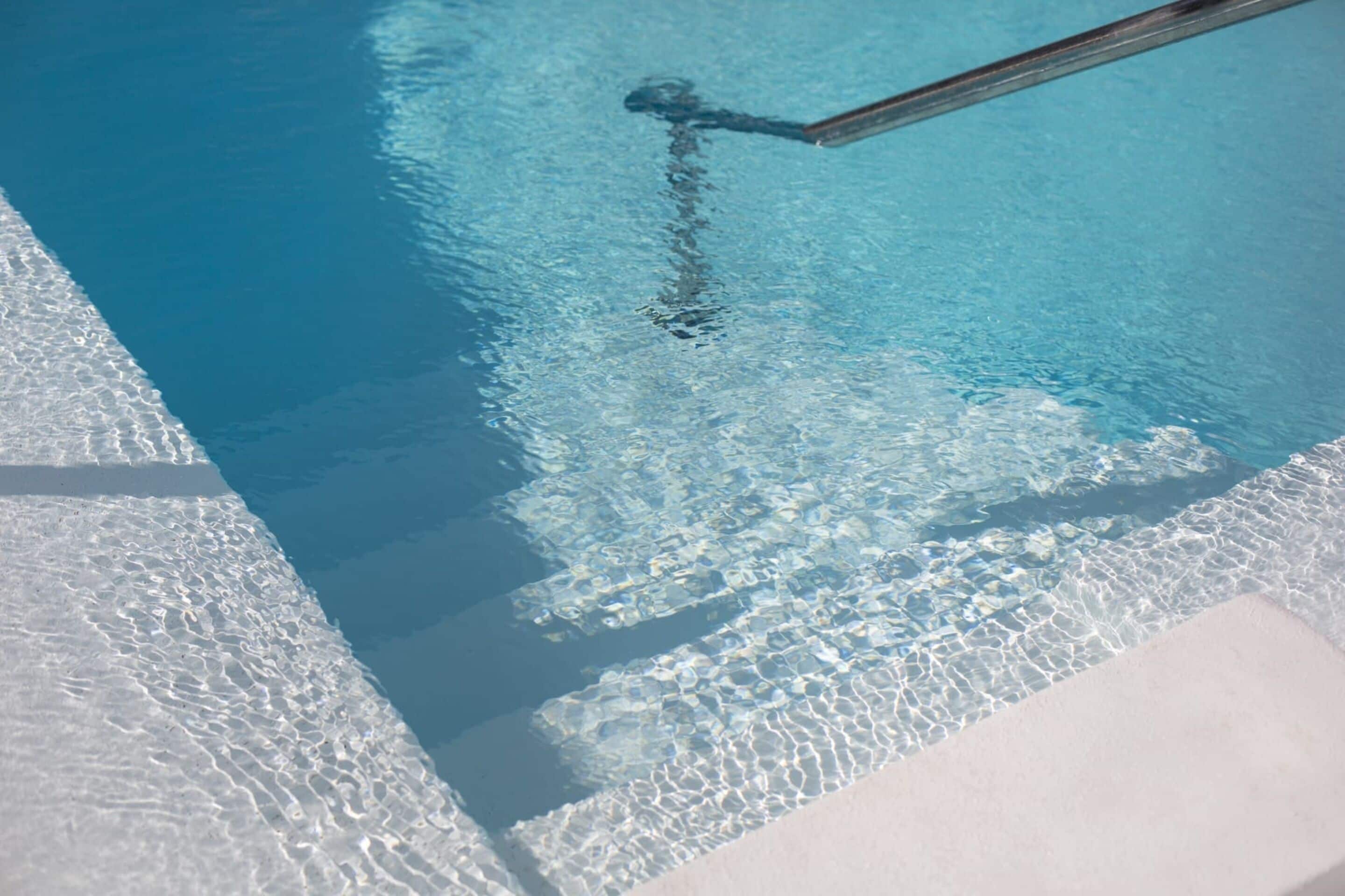 A clear view of a swimming pool with a visible pool ladder and a textured edge.