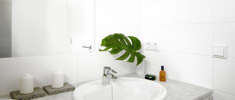 Ein Badezimmer mit einem weißen Waschbecken, einem großen Spiegel und einer Zimmerpflanze.