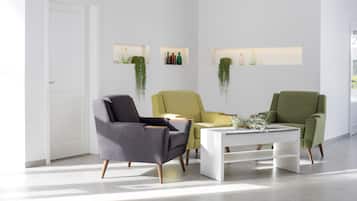 Ein modernes Wohnzimmer mit einer weißen Tür, drei Stühlen, einem weißen Couchtisch und an der Wand befestigten Regalen mit Dekorationen.